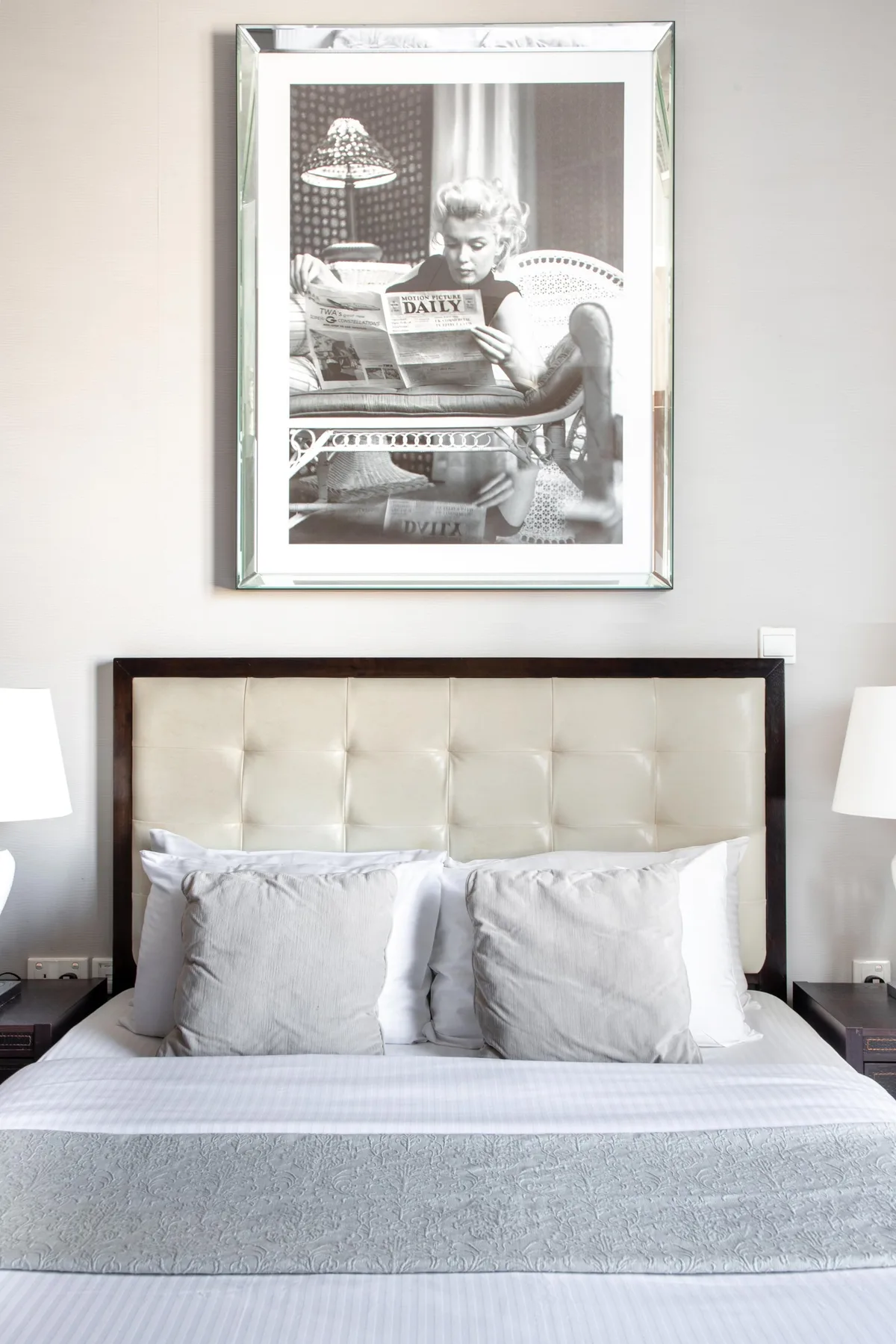 Una cama bien tendida con ropa de cama clara está debajo de una fotografía enmarcada en blanco y negro.