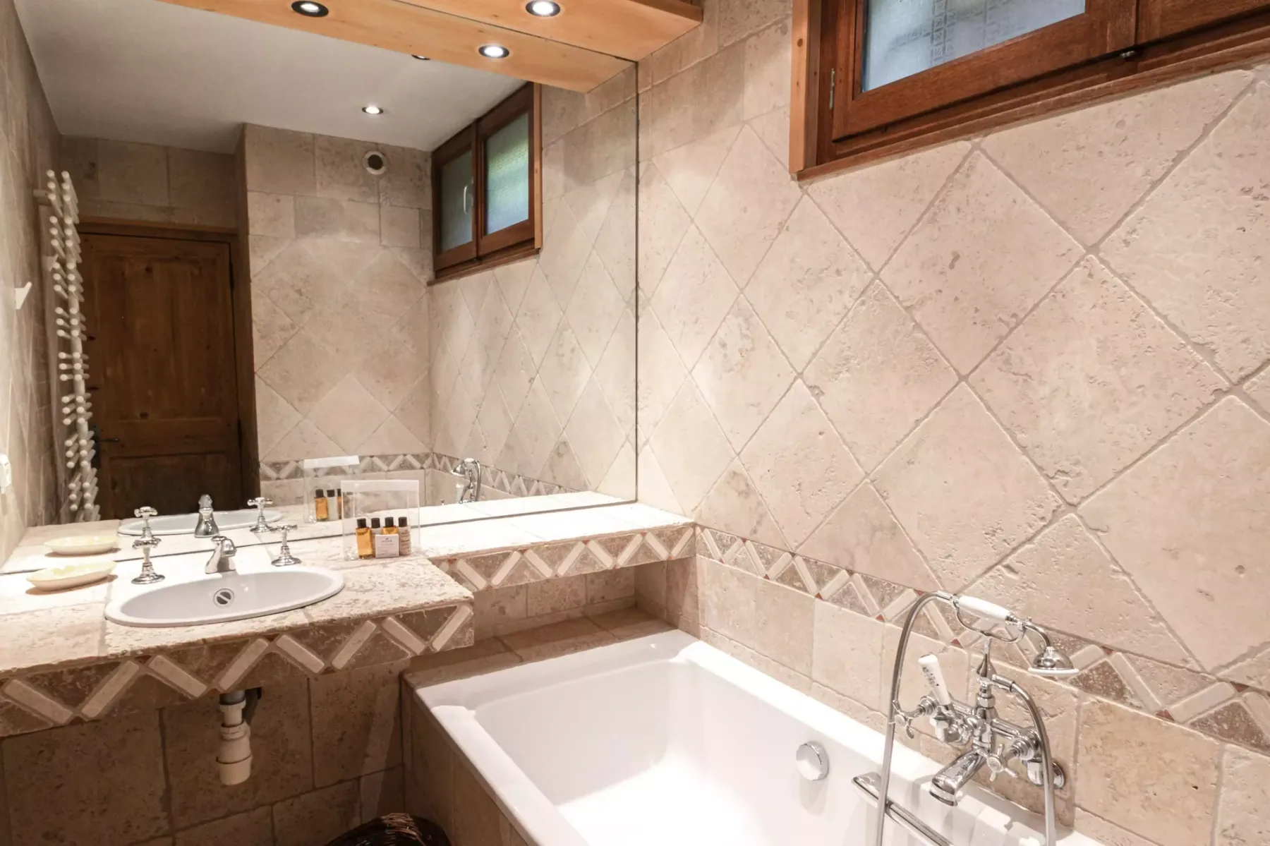 A tiled bathroom with a bathtub, sink, and wall-mounted windows.