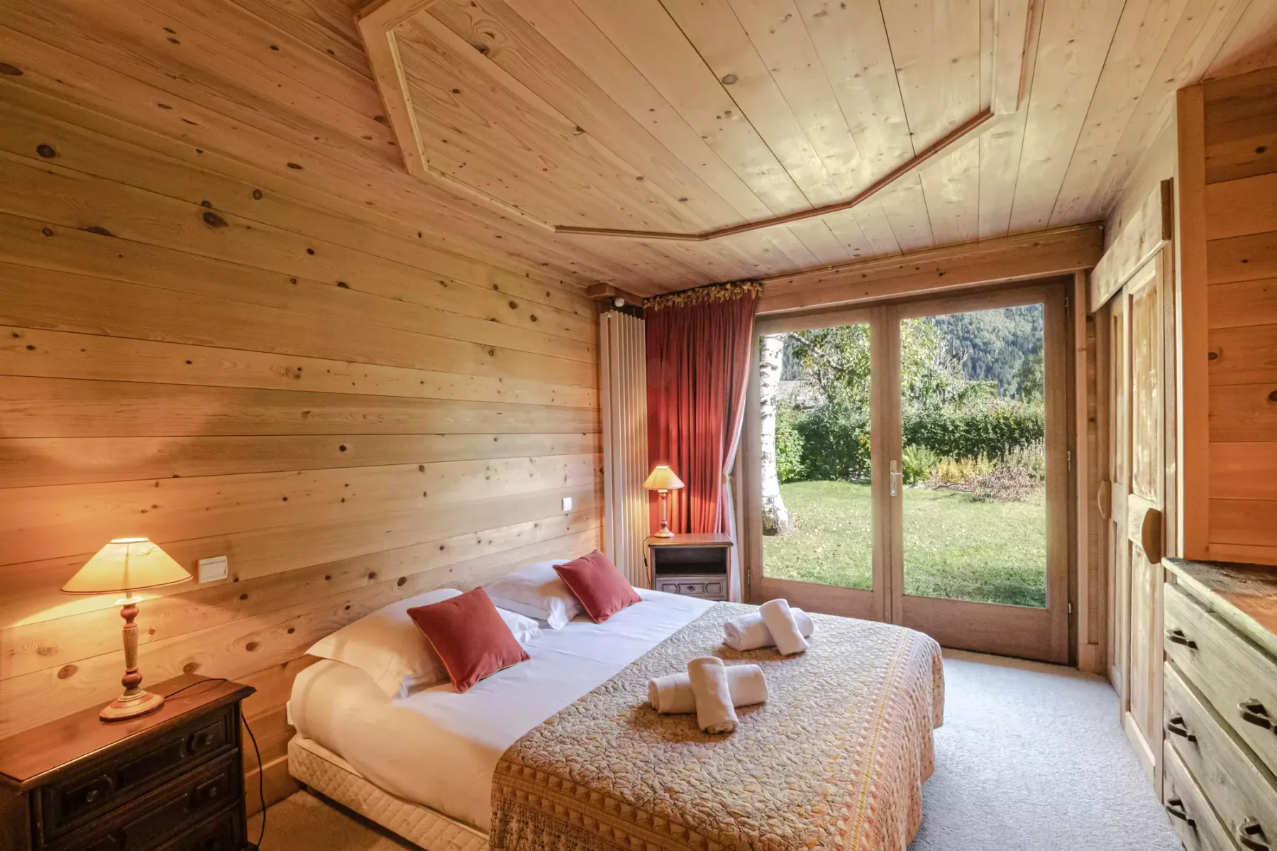 A wood-paneled bedroom with a bed beside glass doors opening onto a garden.