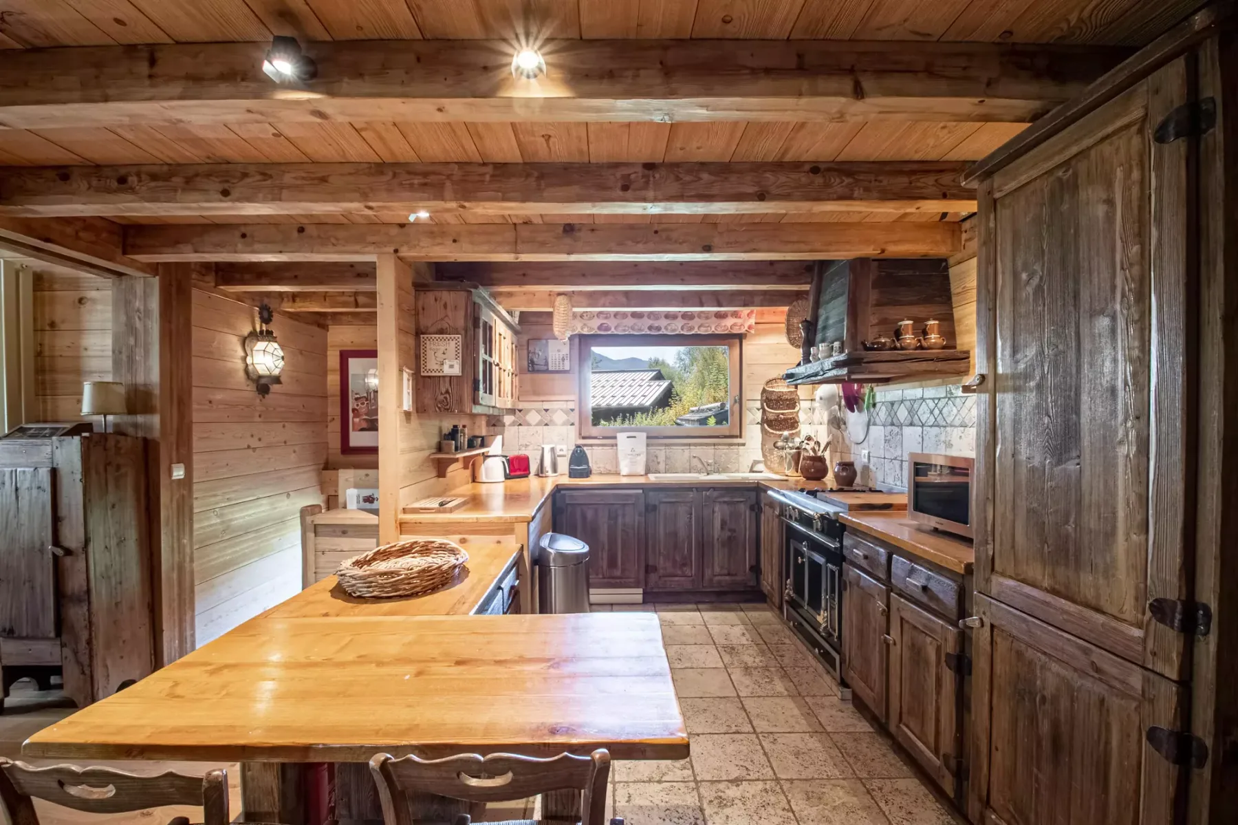 A rustic kitchen with wooden cabinets, a large island, and exposed beams.