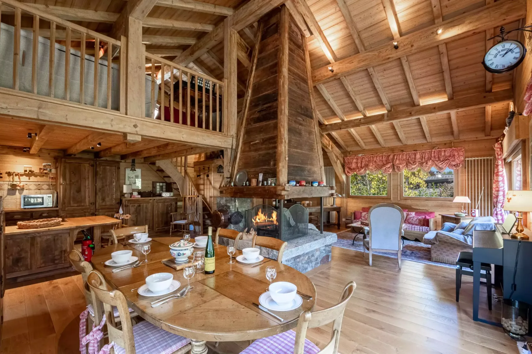 A timber lodge interior combines a dining area with a lounge around a central fireplace.
