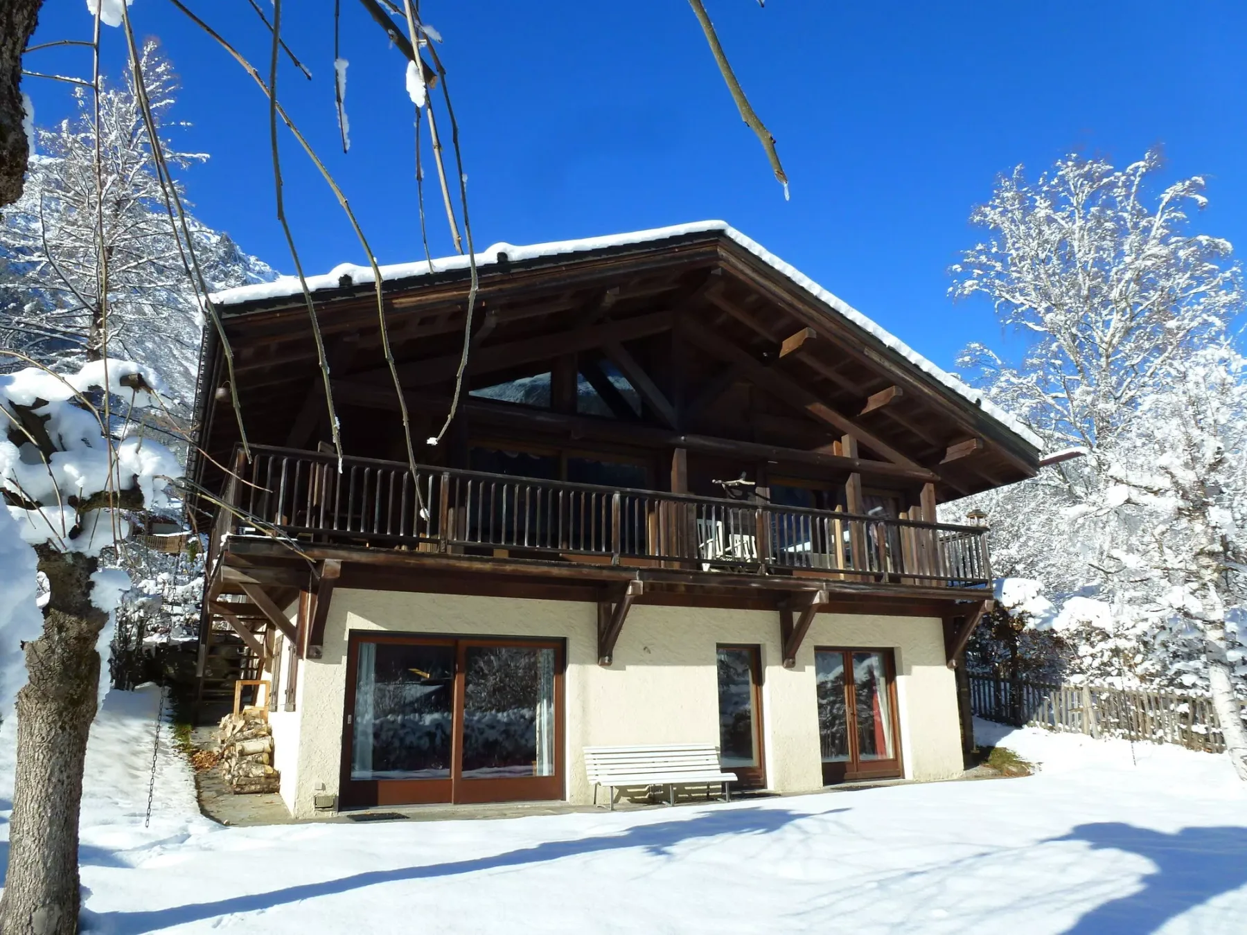 A chalet-style house stands in a snowy landscape beneath a clear blue sky.