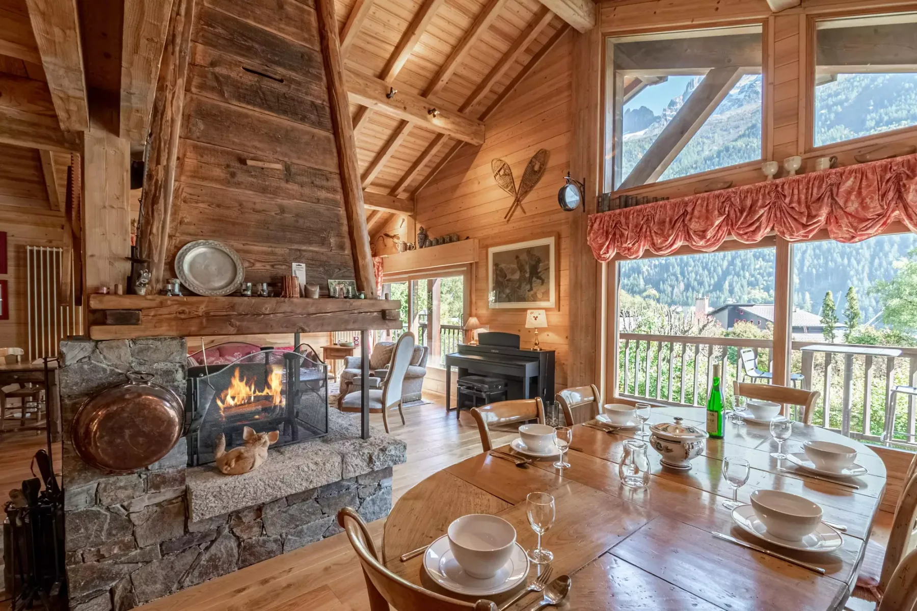 A wood-paneled dining room with a stone fireplace and mountain views through large windows.