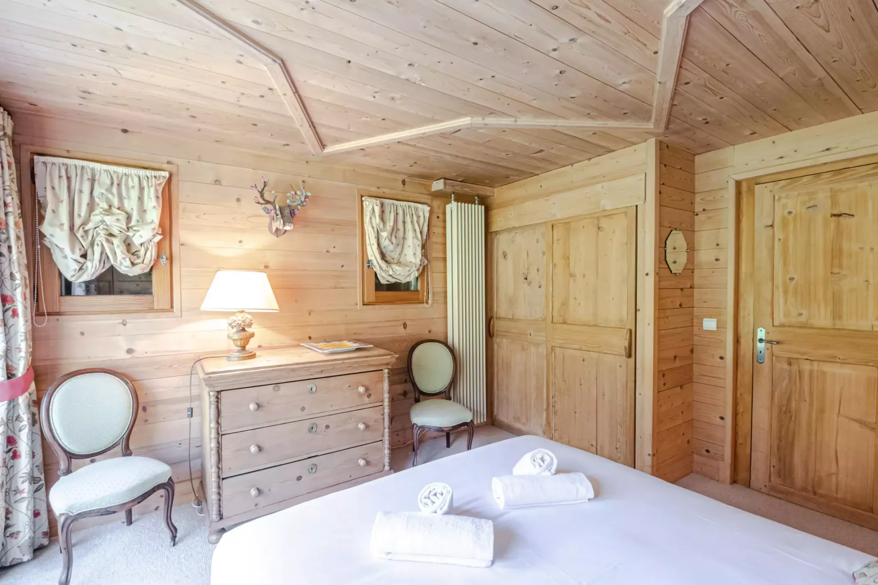 A wood-paneled bedroom with a bed, dresser, and two wooden doors.