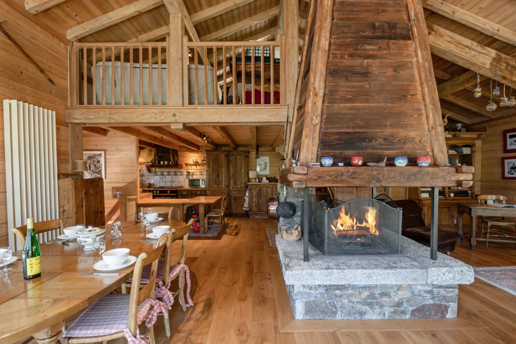 A wood-paneled dining and living area features a large stone fireplace with a burning fire.