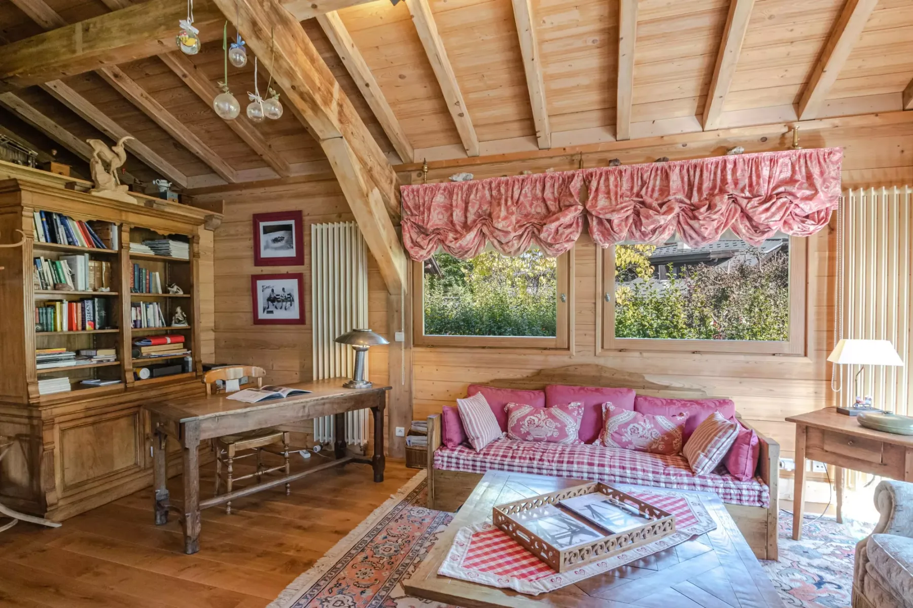 A wood-paneled living room with a patterned sofa beneath two windows.