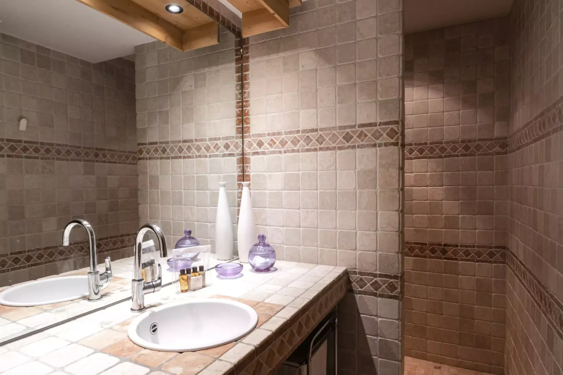 A tiled bathroom vanity with two sinks and decorative bottles.