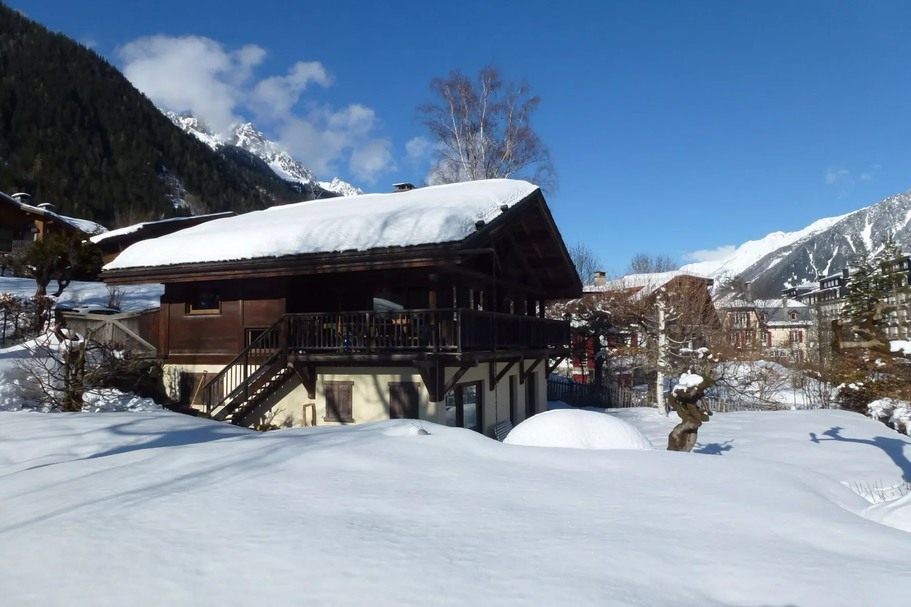 A wooden chalet stands in a snowy mountain setting beneath a clear blue sky.