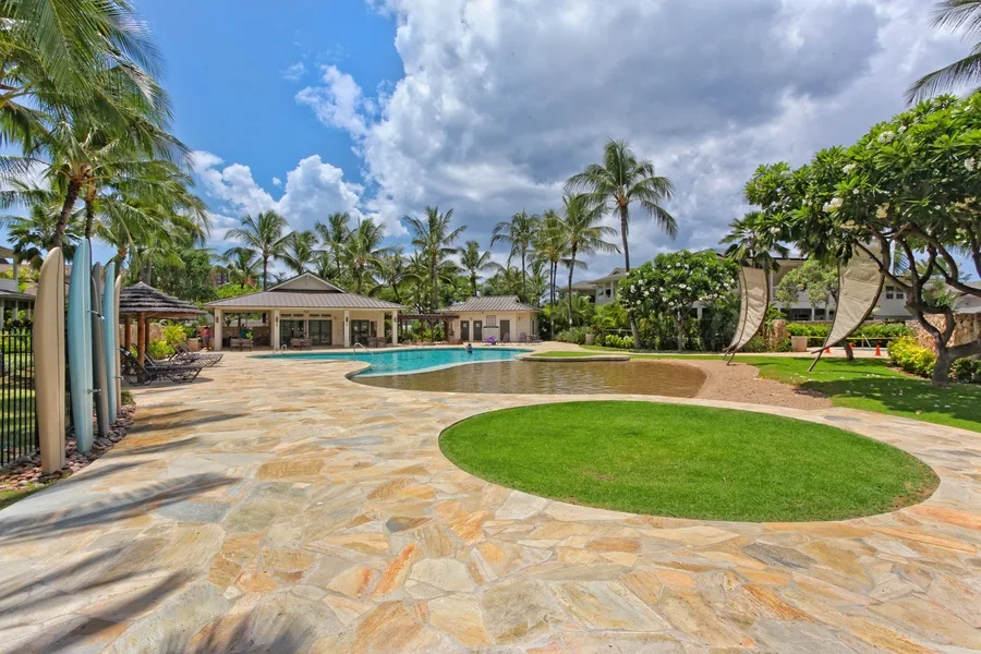 Una piscina tropical está junto a una terraza de piedra y un césped verde.