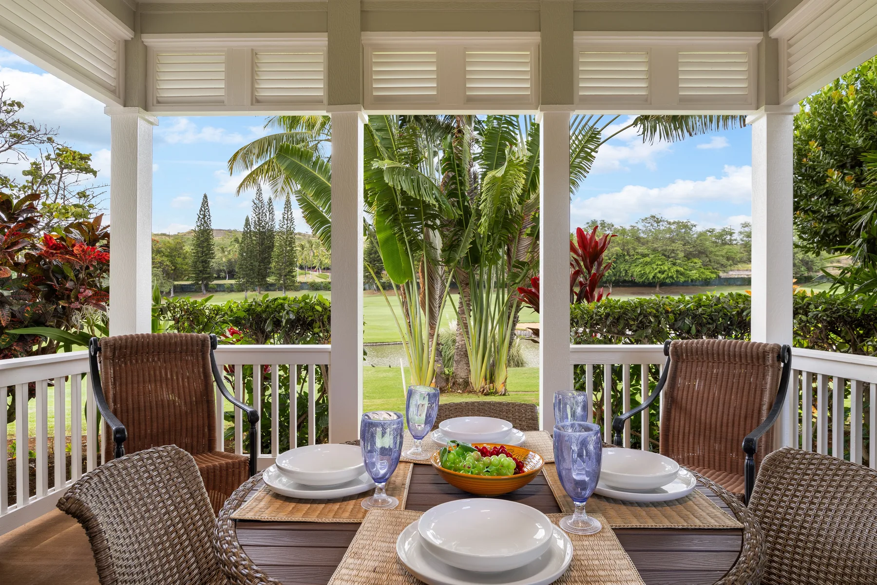 Una zona de comedor exterior cubierta da a vegetación tropical, con una mesa puesta y asientos tejidos.