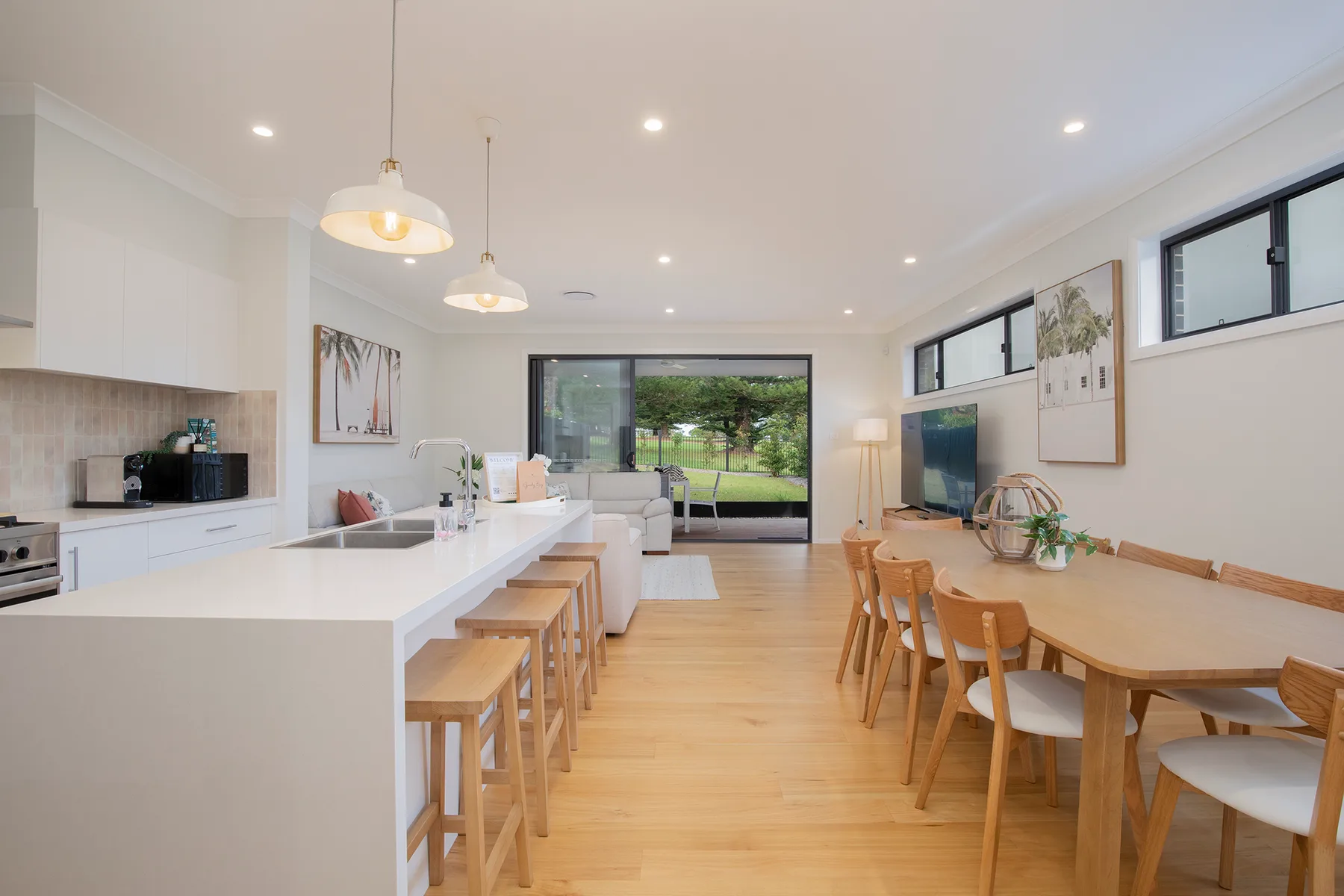 Una cocina y comedor de planta abierta tienen una mesa larga y grandes ventanas con vistas a zonas verdes.