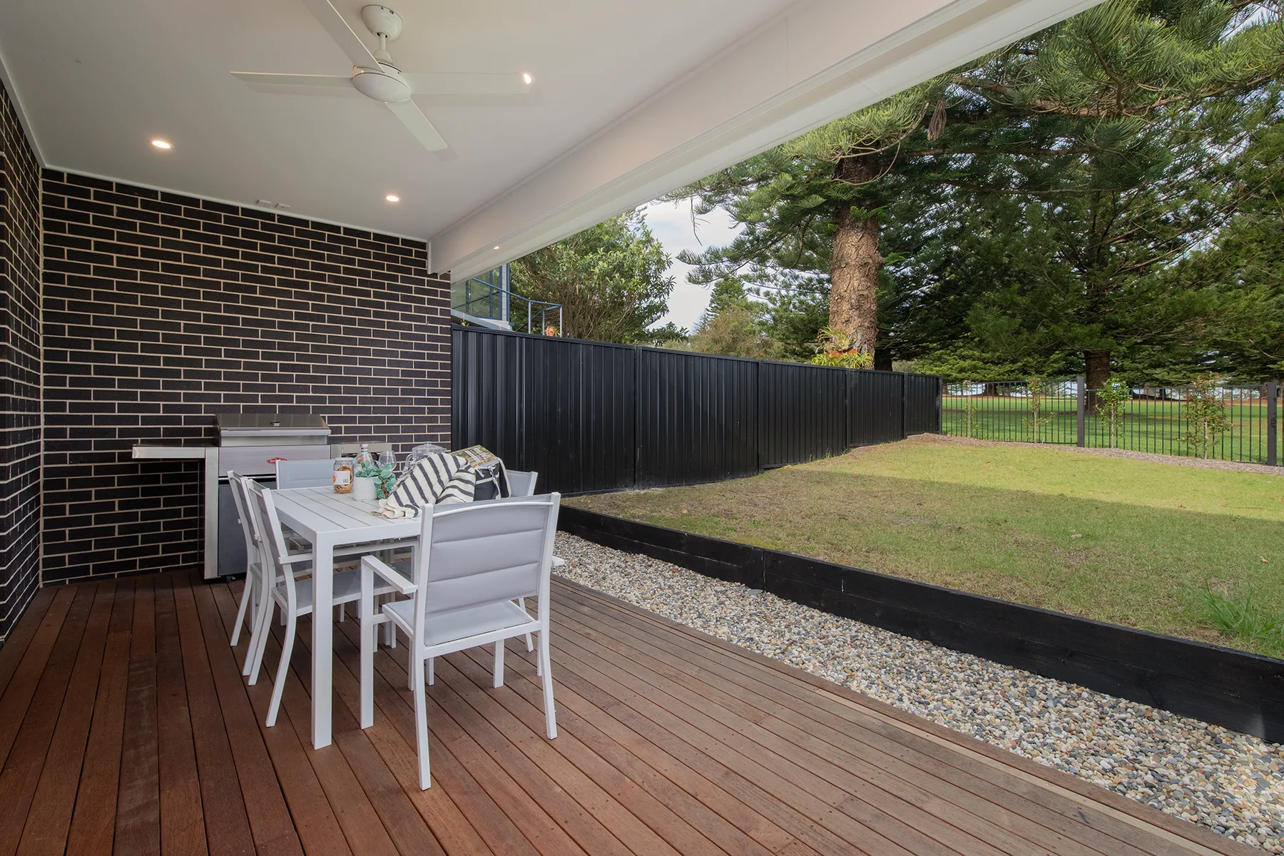 Un patio cubierto tiene asientos de comedor al aire libre junto a un patio con césped y cercado.