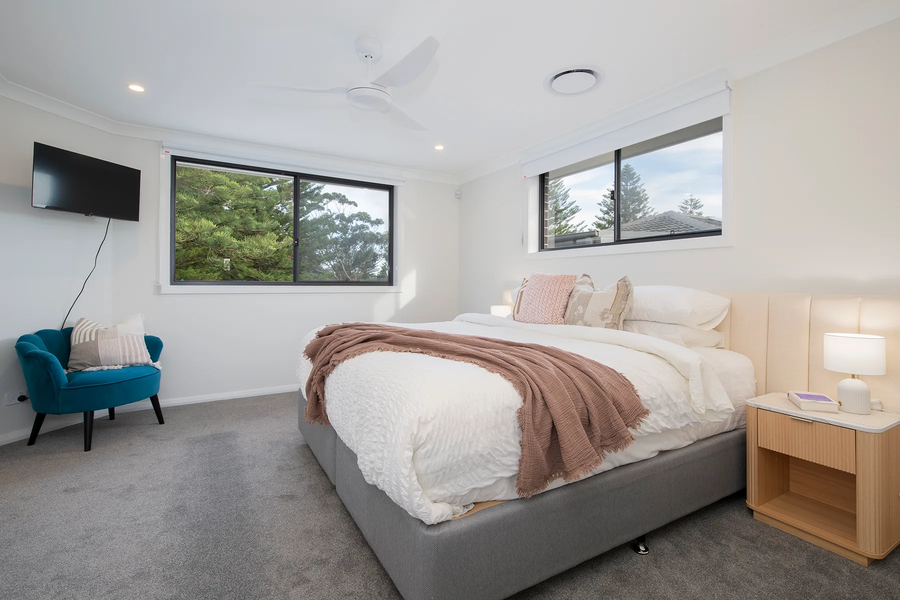 Un dormitorio con una cama grande, un televisor montado en la pared y vistas frondosas por las ventanas.