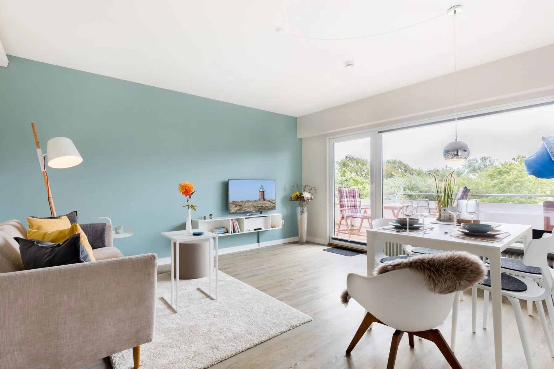 A bright living and dining area opens onto a balcony through large glass doors.