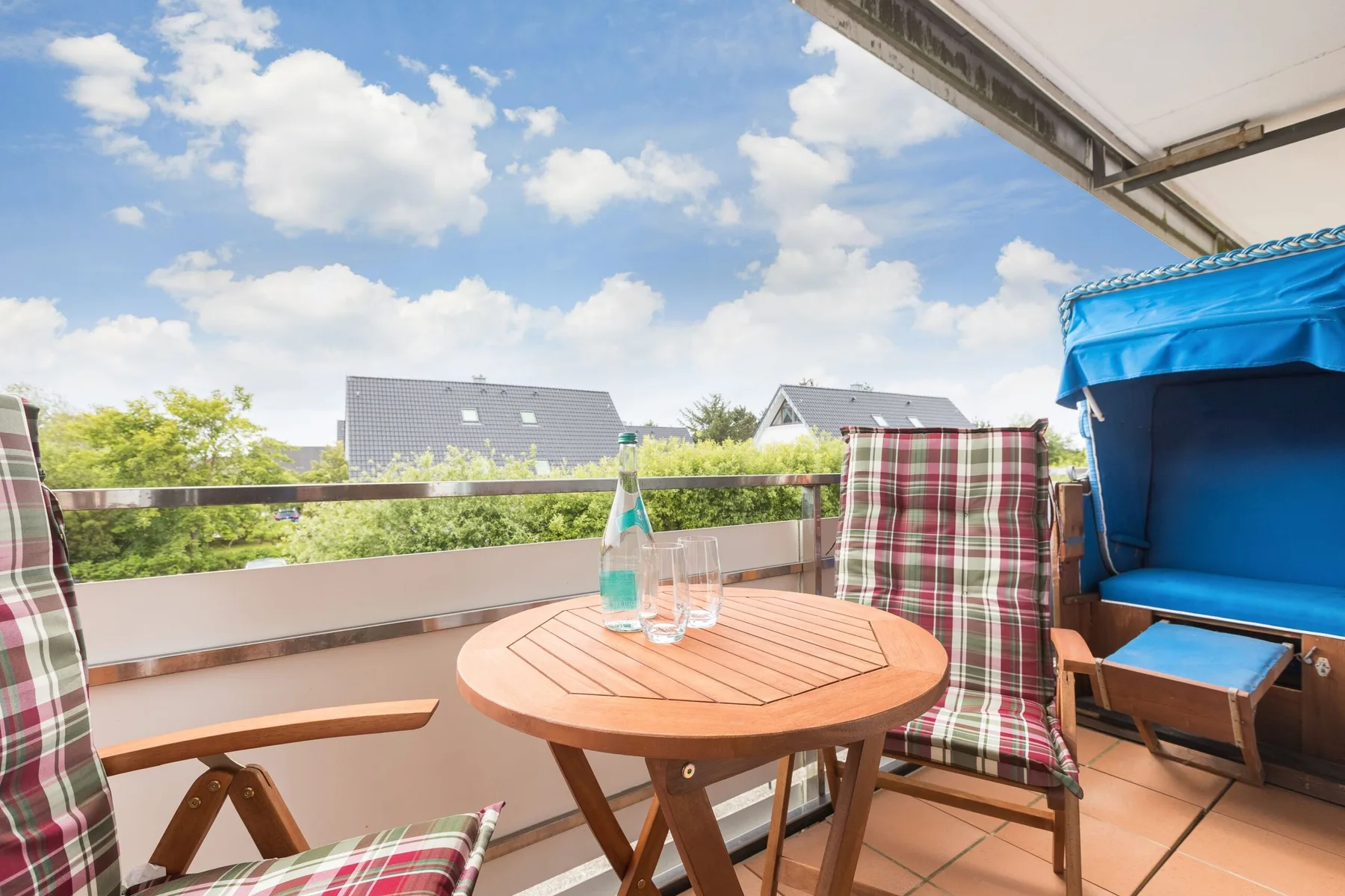 A furnished balcony with a round wooden table overlooking nearby rooftops.
