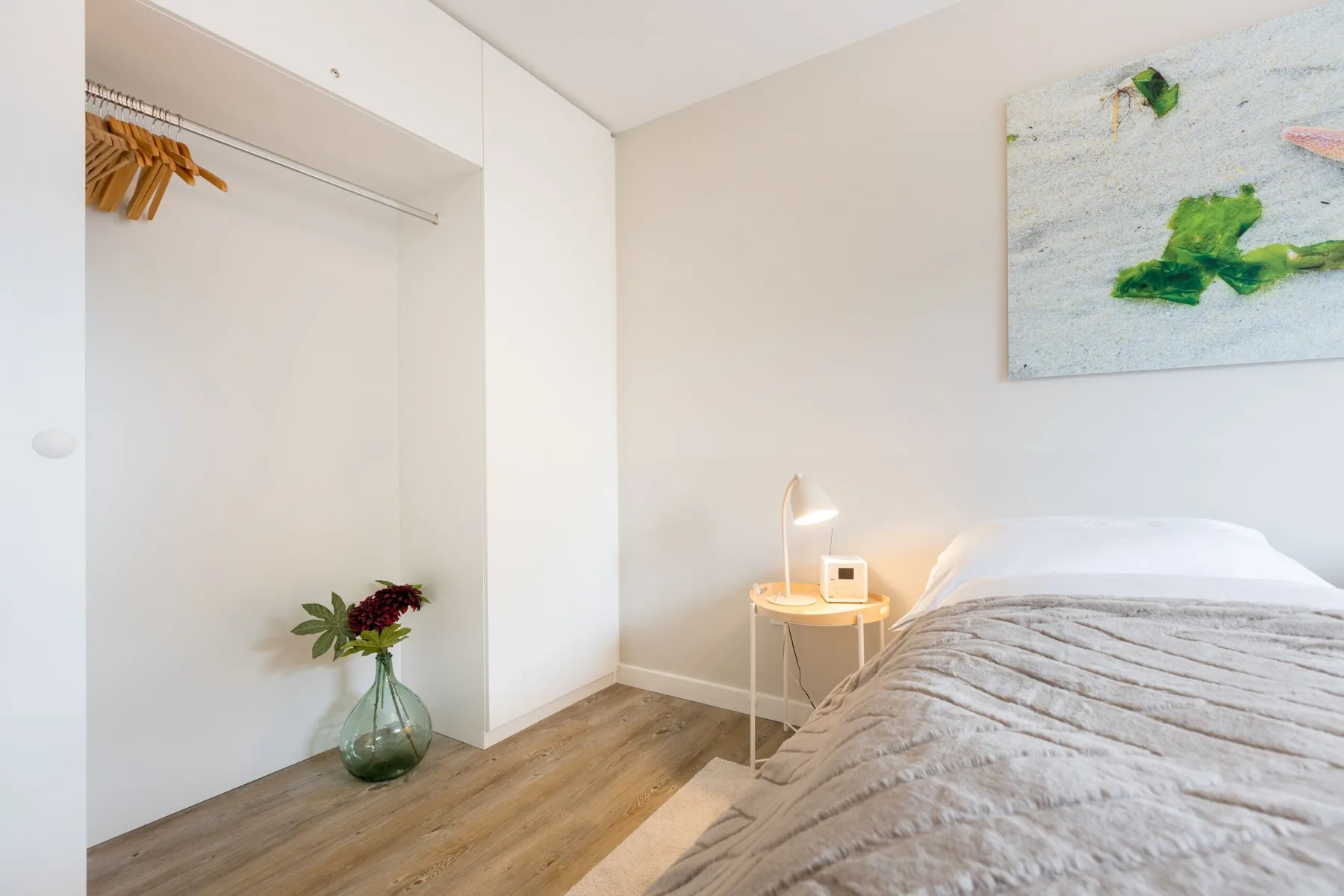 A bright bedroom with a bed, bedside table, and open clothes rail.