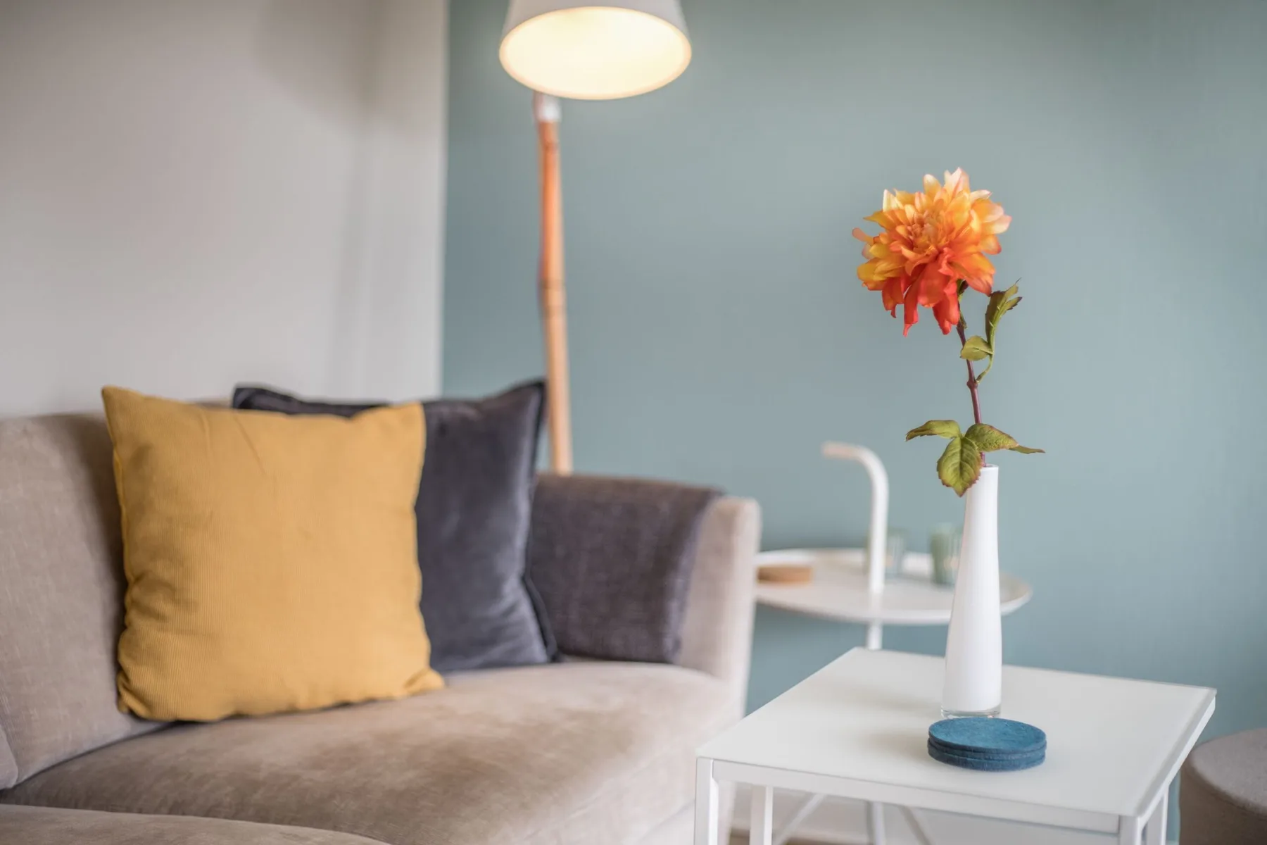 A living room seating area with a yellow cushion and a flower on the table.