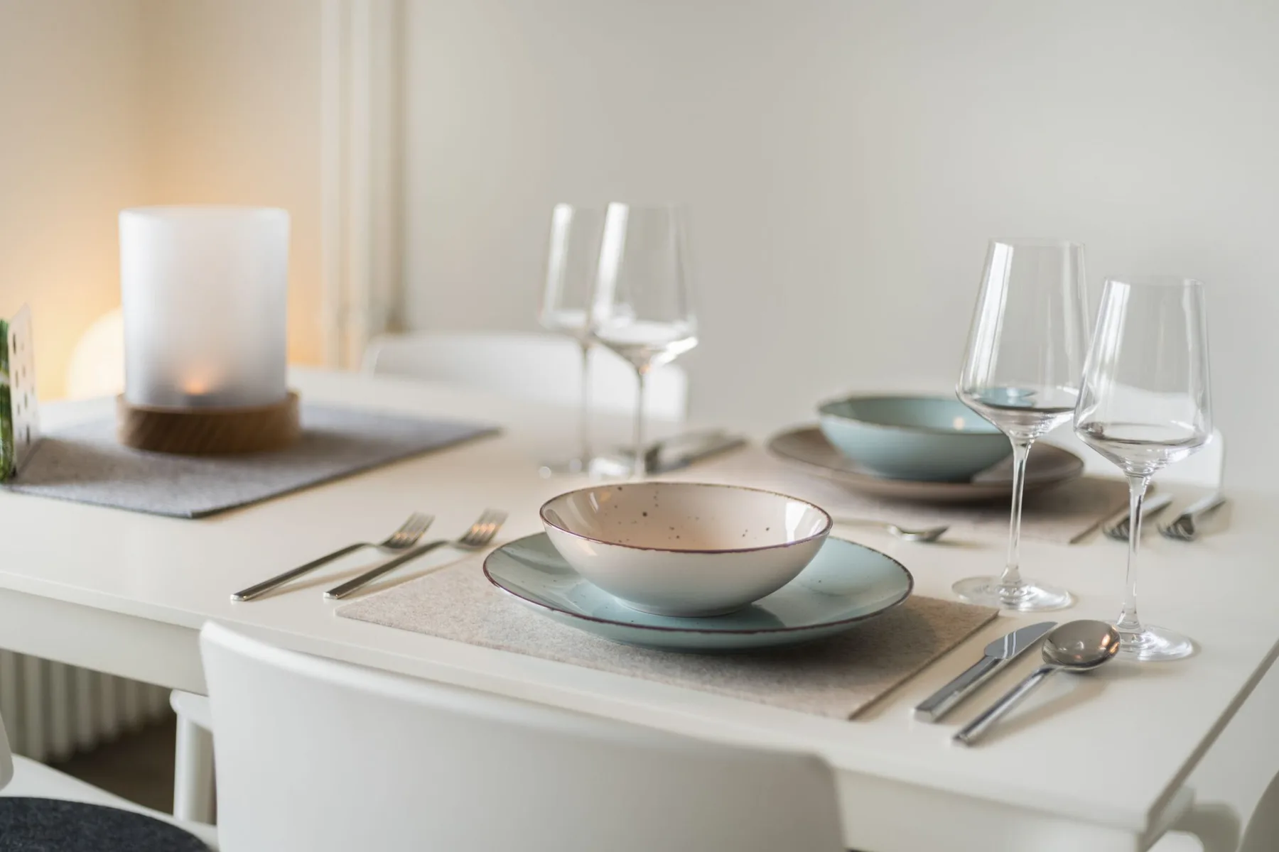 A dining table is set with plates, bowls, cutlery, glasses, and a candle.