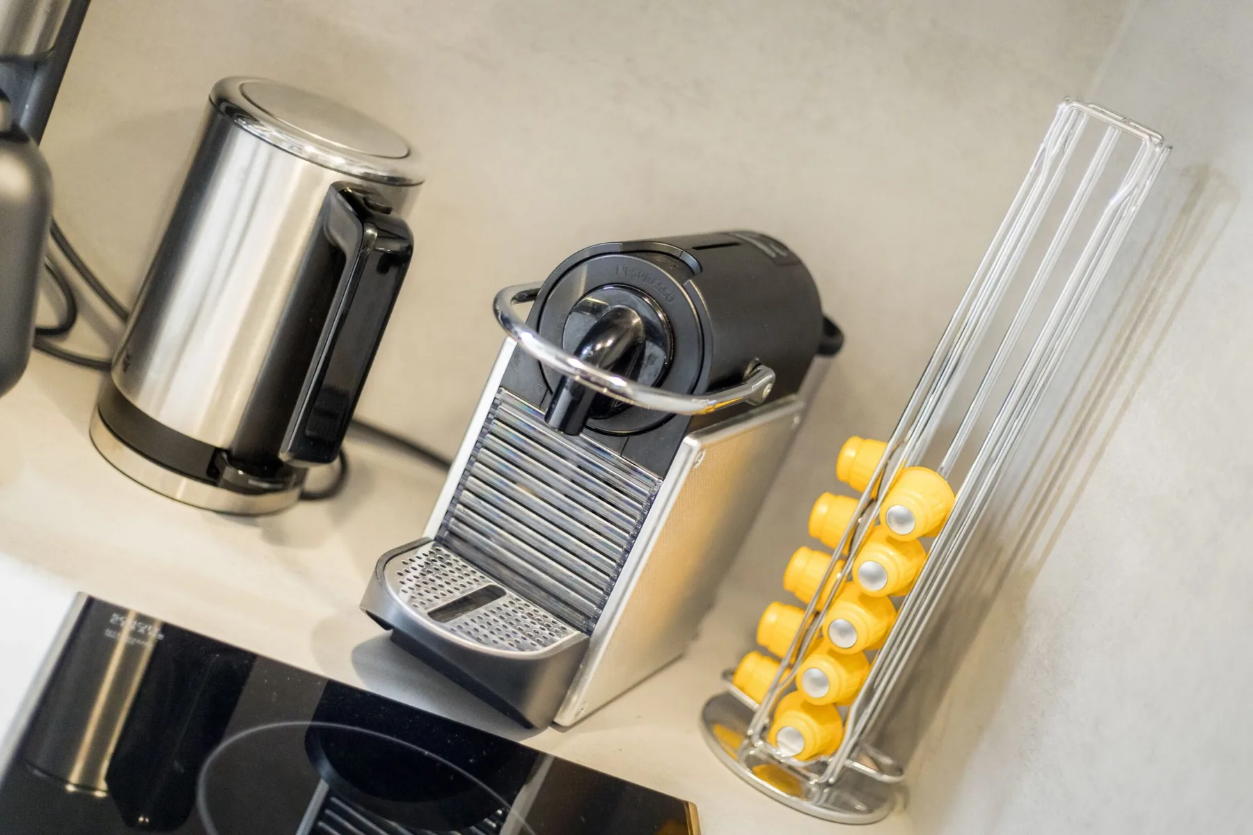 A kitchen counter with a coffee machine, kettle, and coffee capsules.