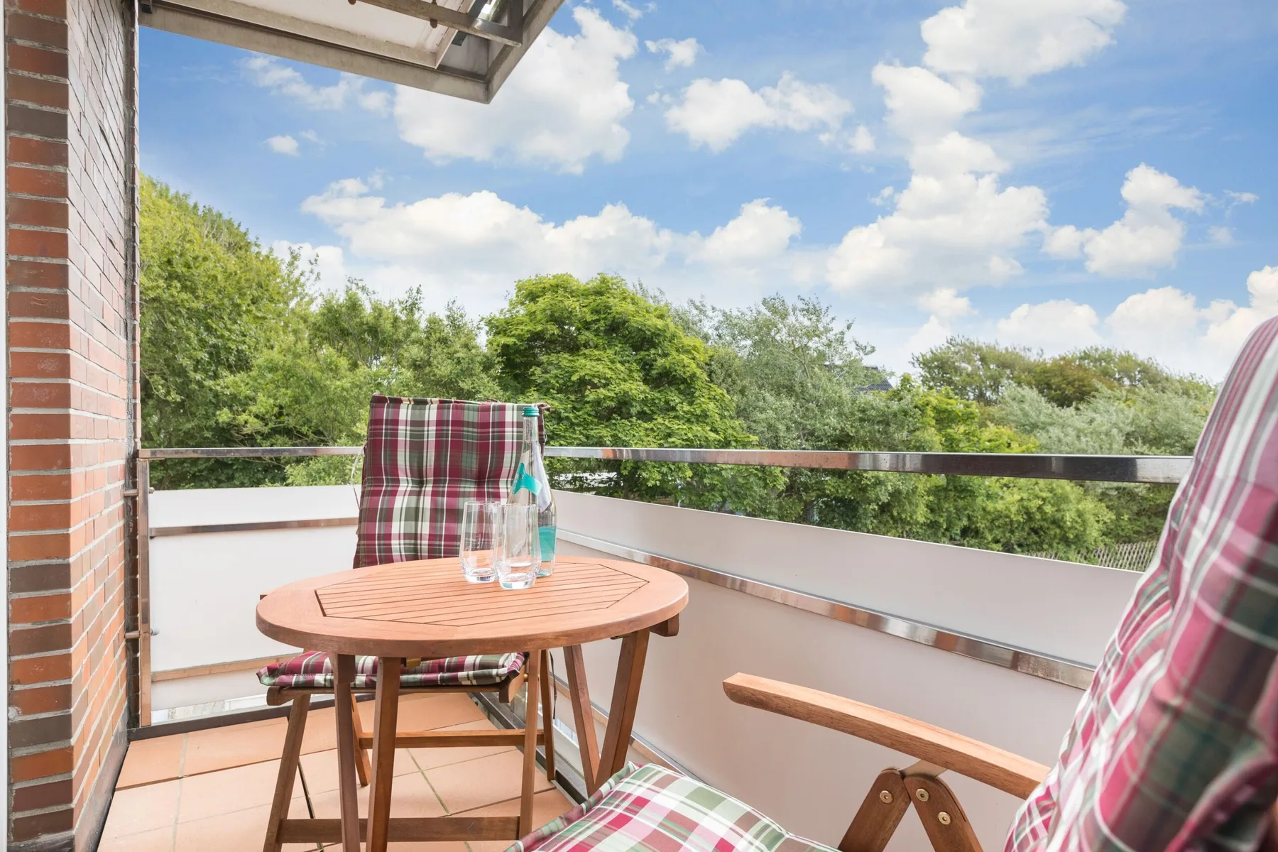 A balcony seating area with a round table overlooking leafy trees.