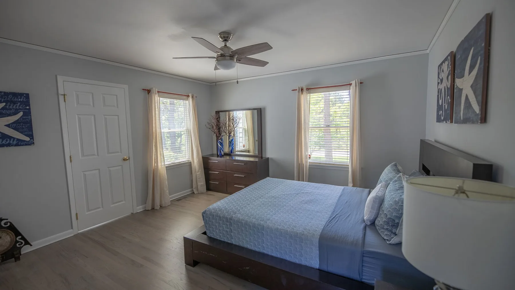A bedroom with a bed, dresser, and two windows.