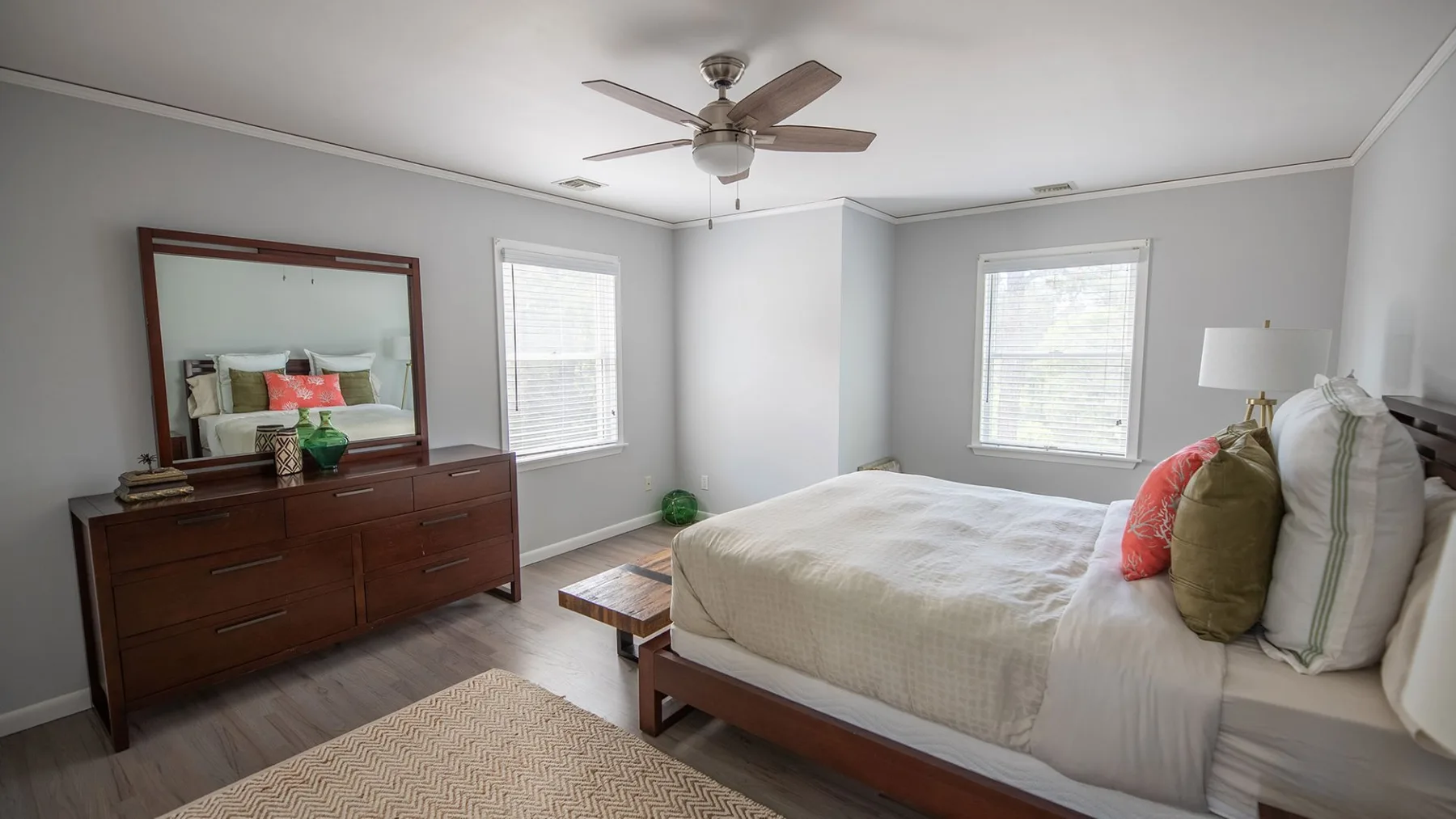 A bedroom with a large bed, wooden dresser, and ceiling fan.