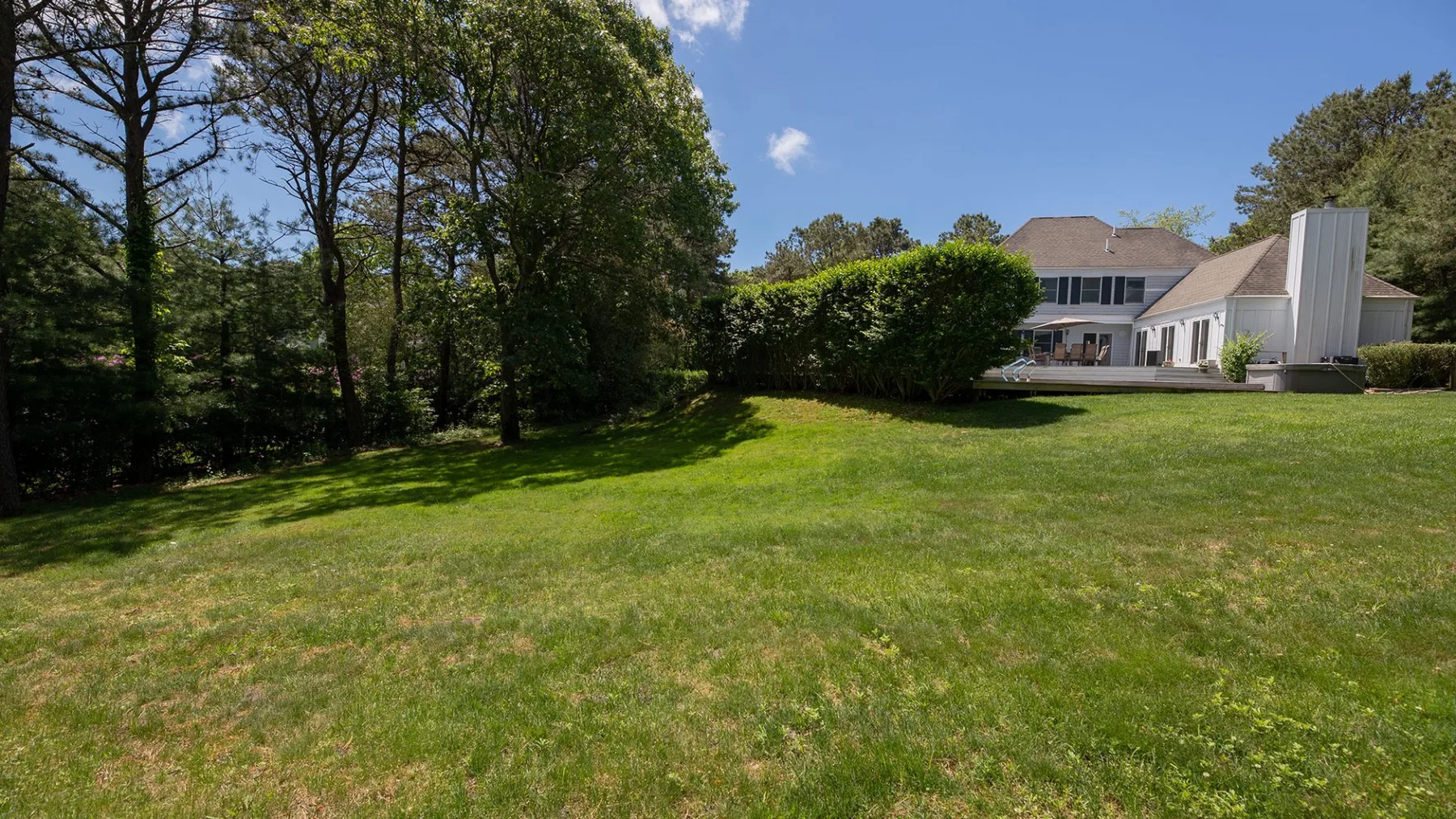 A broad grassy lawn stretches toward a house and surrounding trees.