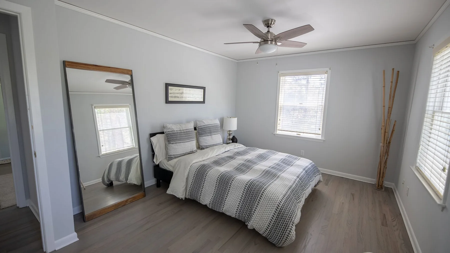 A bedroom with a bed, a full-length mirror, and windows.