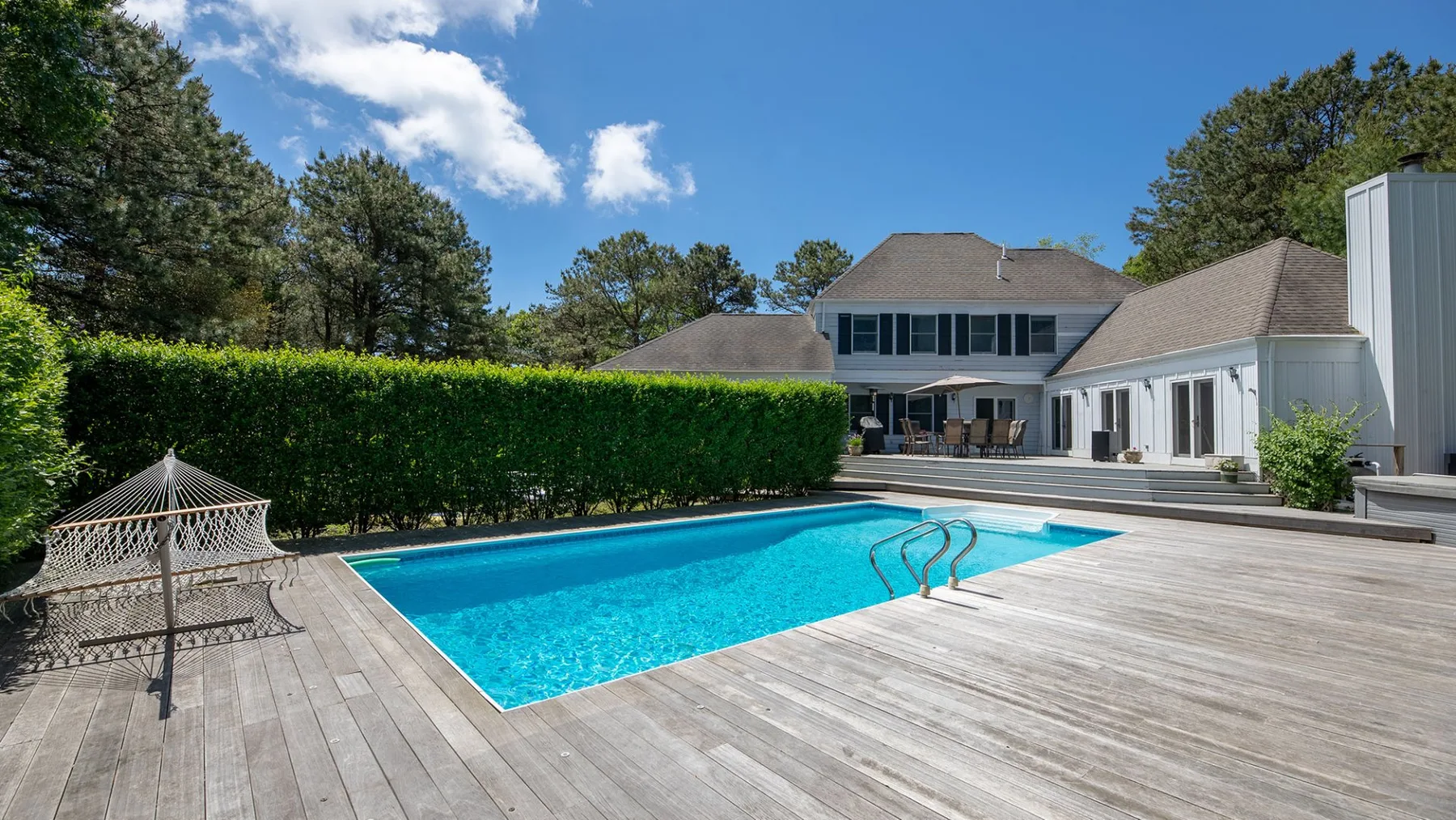Outdoor swimming pool beside a broad wooden deck and a house.