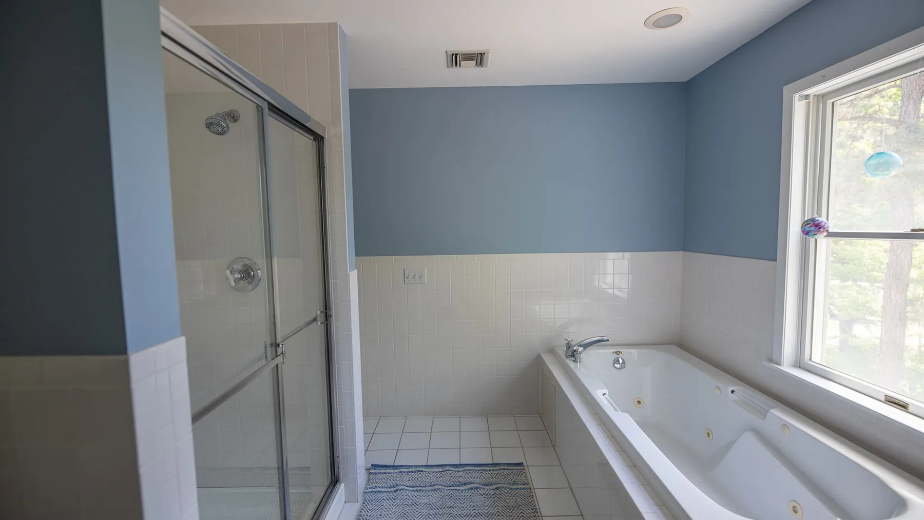 A bathroom with a glass-enclosed shower and a bathtub beside a window.