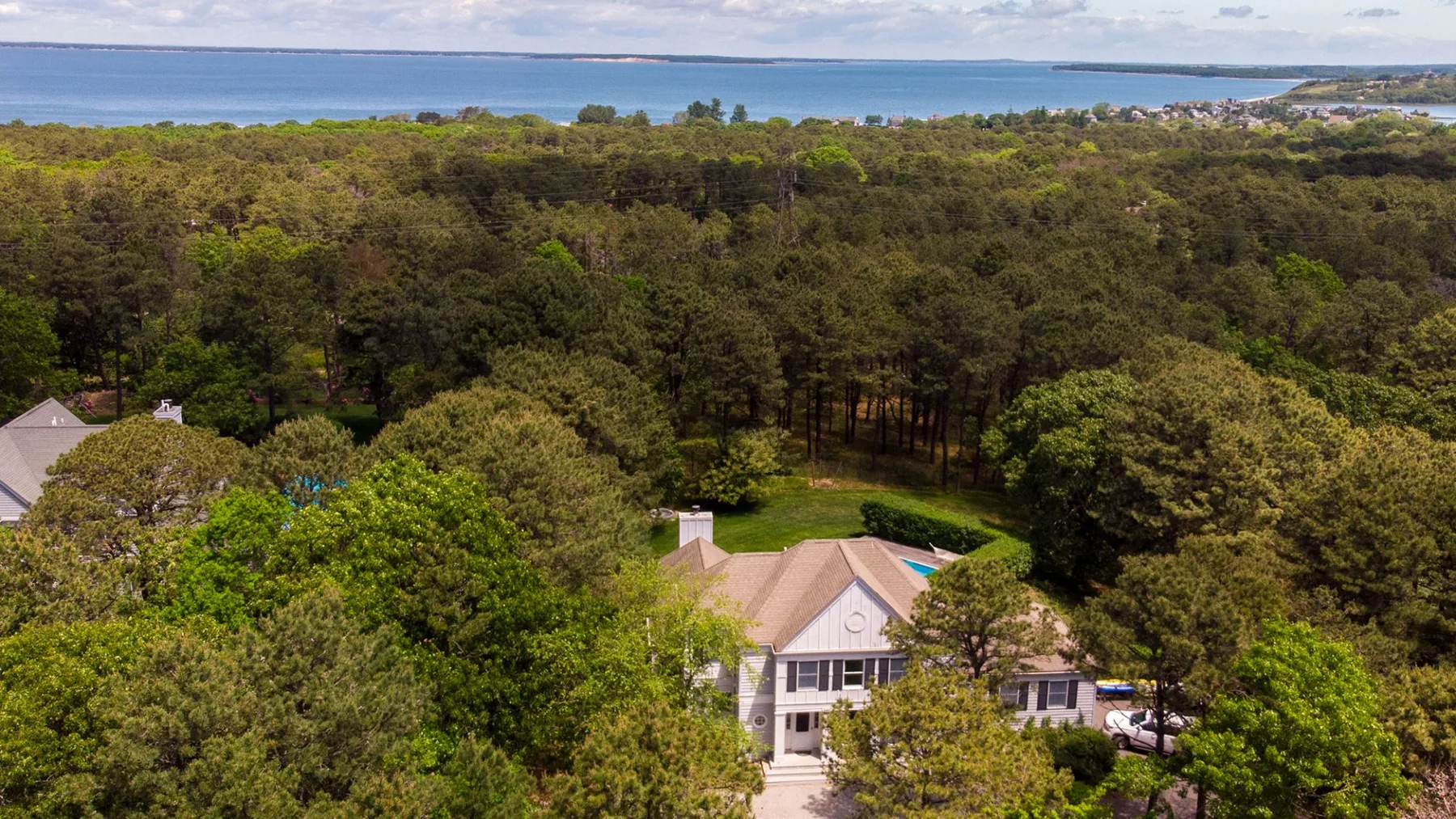 Aerial view of a house among trees, with a bay visible in the distance.