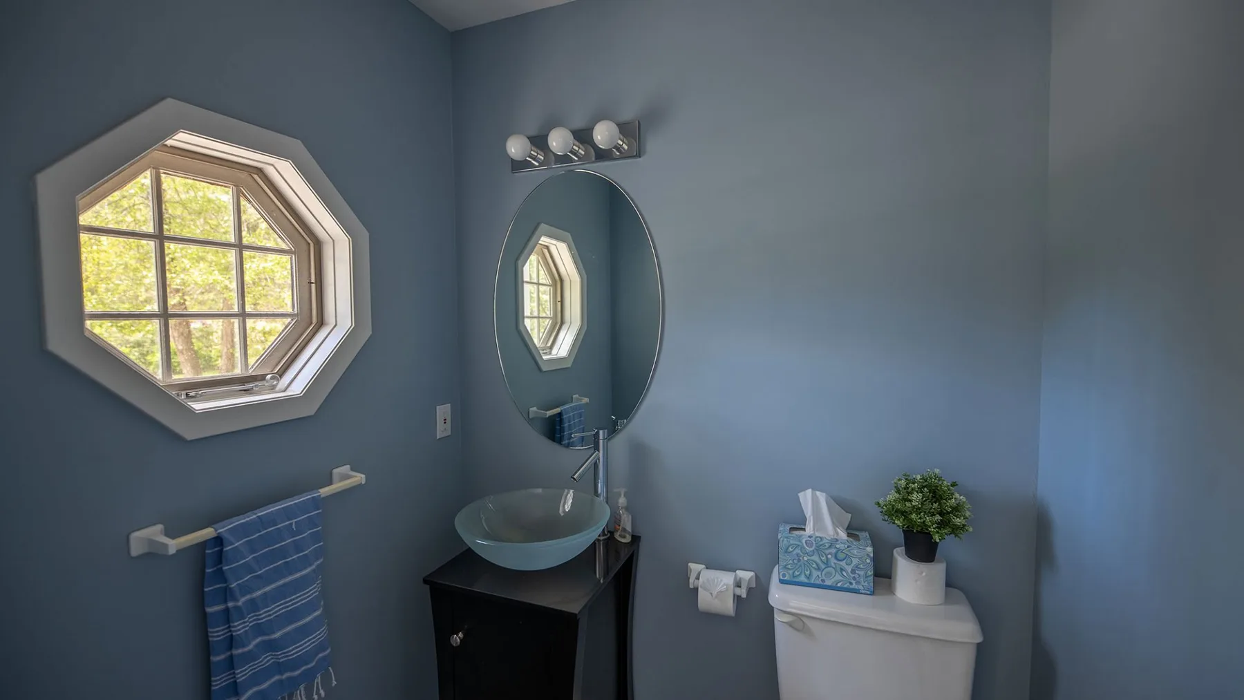 A blue bathroom with a sink, mirror, and window.