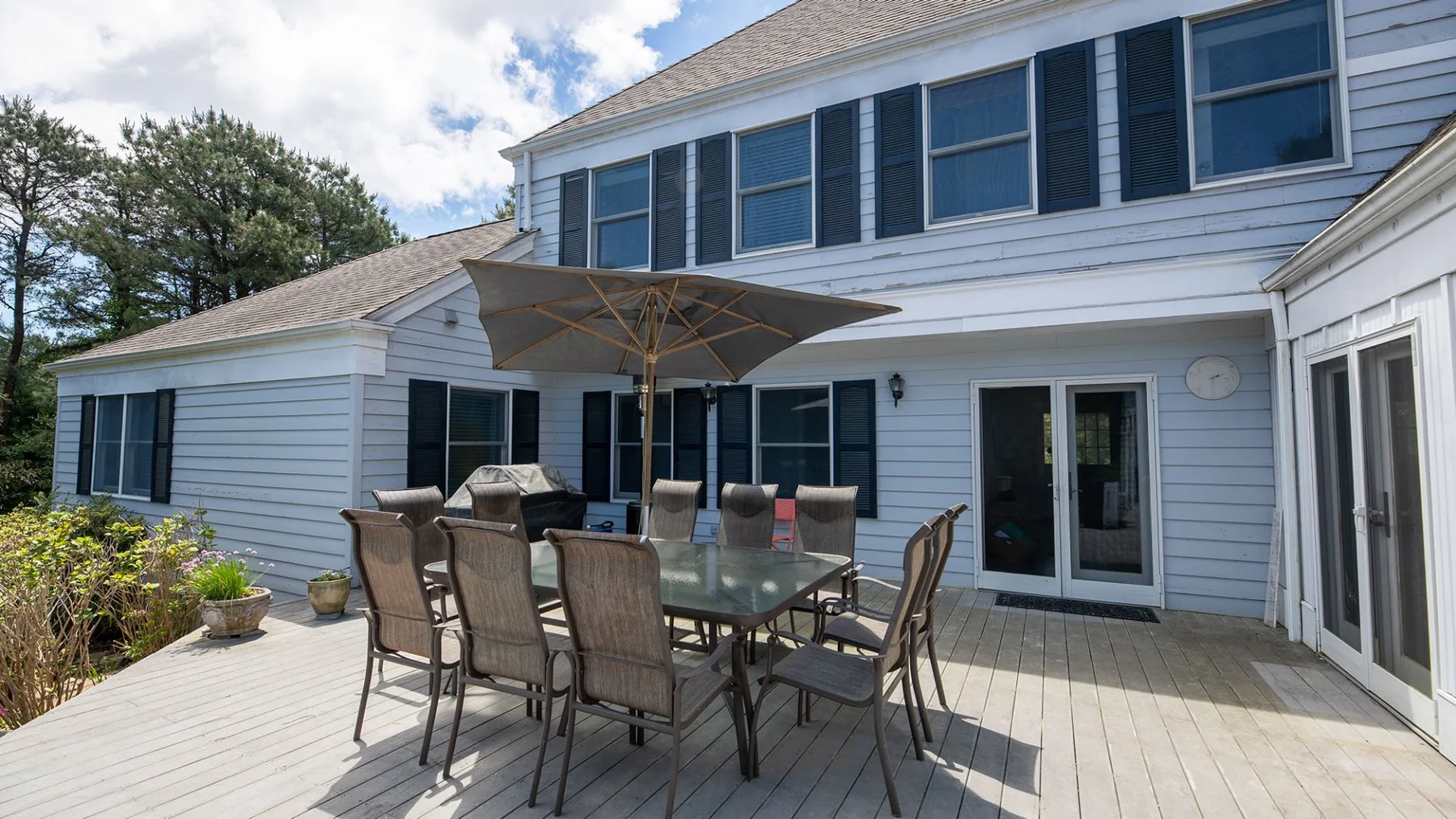 A sunny outdoor patio with a dining table and umbrella beside a house.