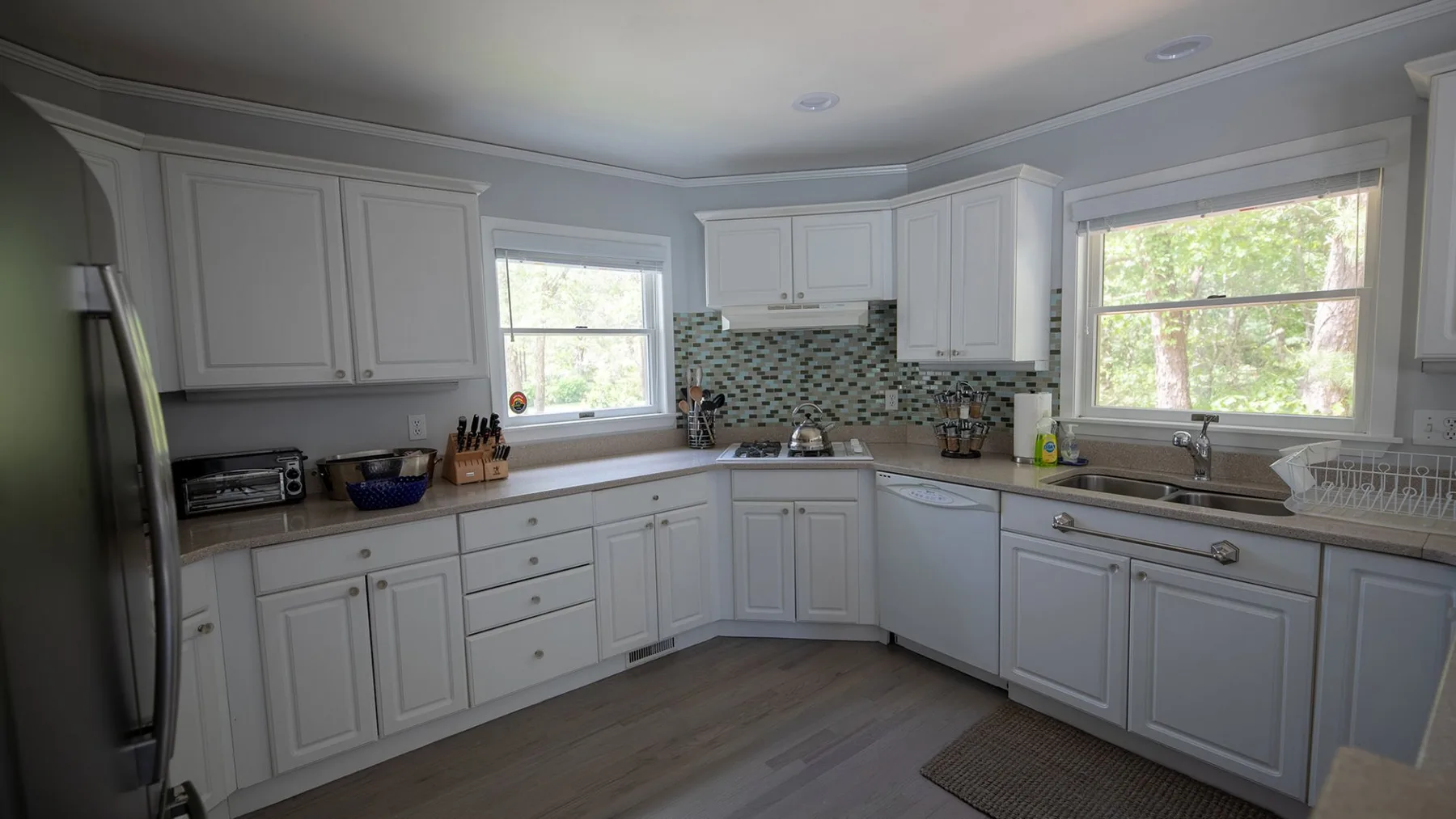 A bright kitchen with white cabinets, a tiled backsplash, and windows.