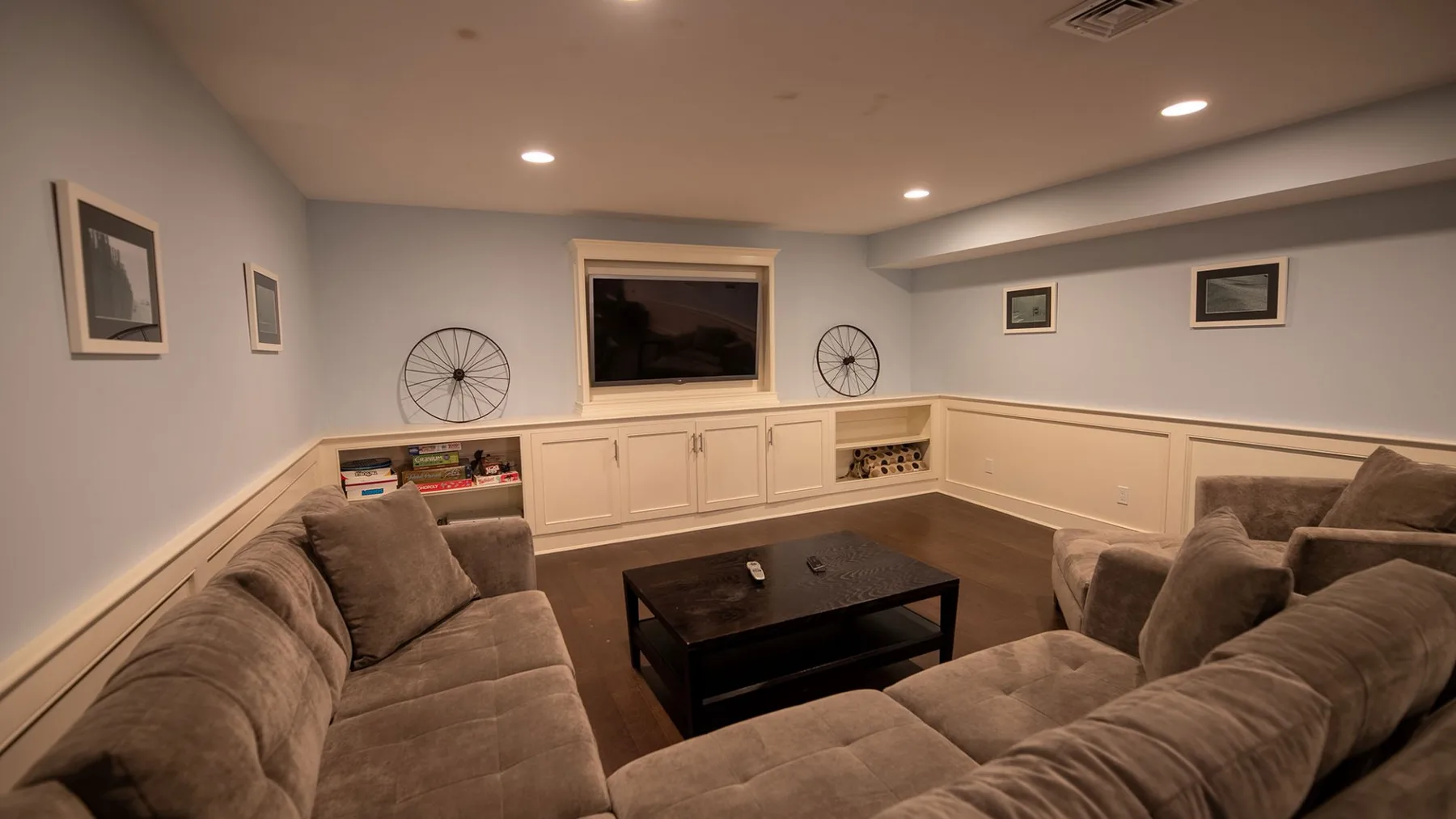 A basement lounge with upholstered seating, a coffee table, and a television.