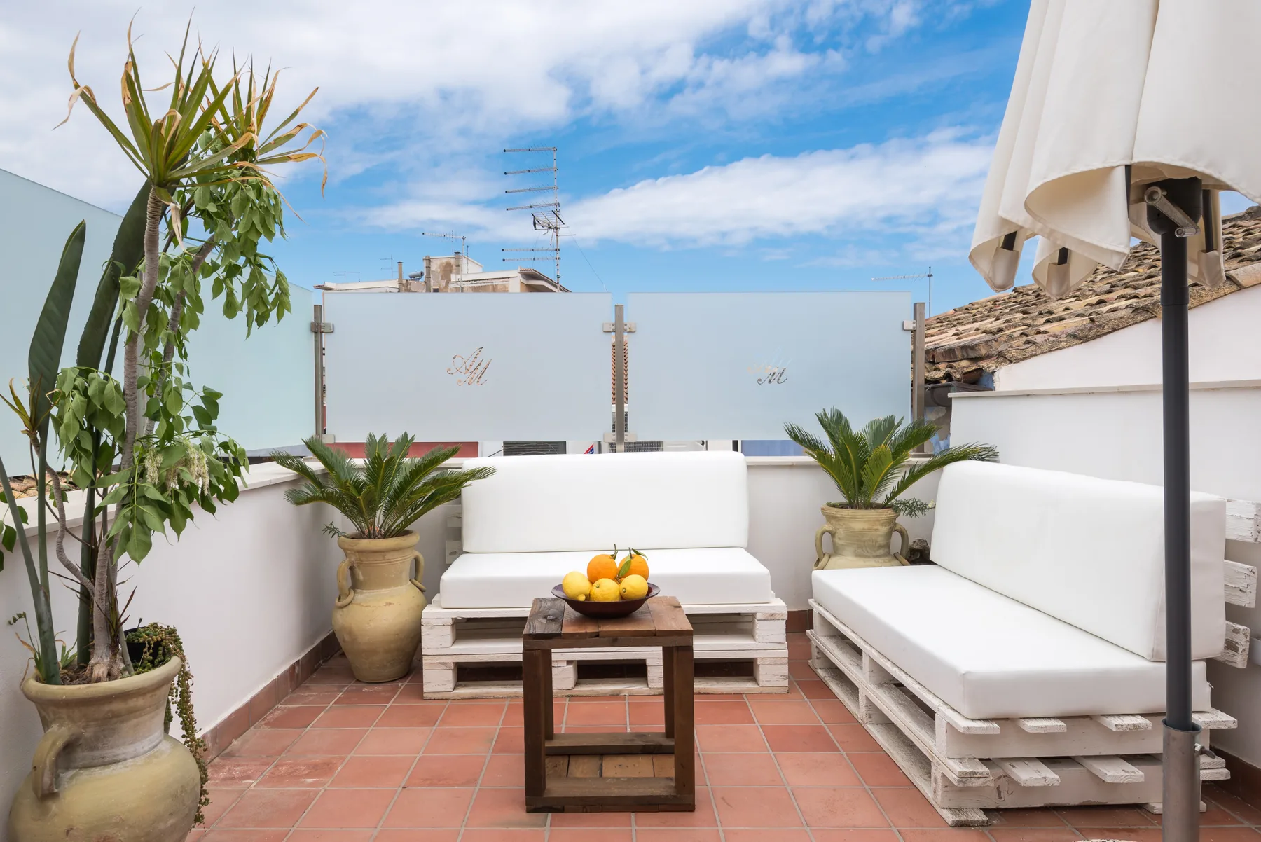 A rooftop terrace with white seating, potted plants, and a small table.