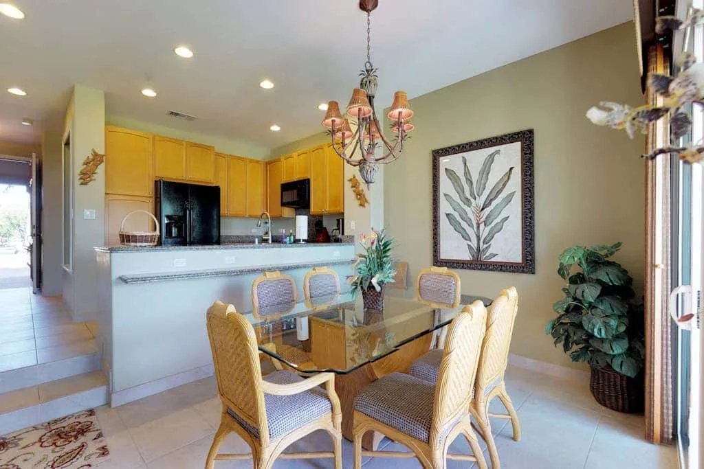A dining area with a glass table and wicker seating beside an open kitchen.