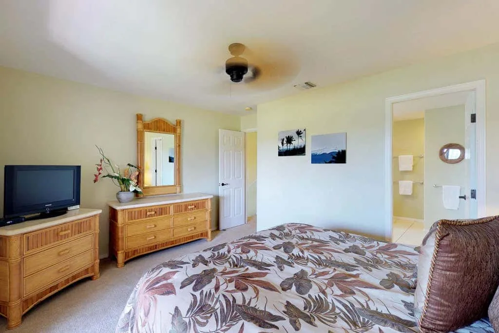 A bedroom with a patterned bedspread, wooden dresser, and open doorway.