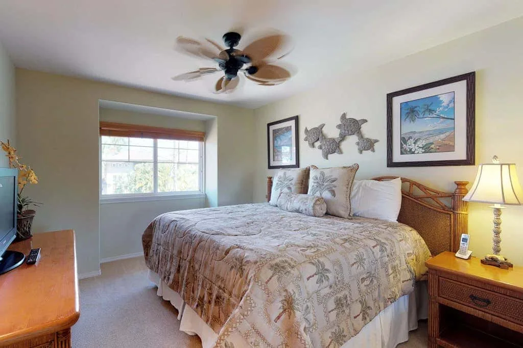 A bedroom with a bed beneath framed artwork and a ceiling fan.