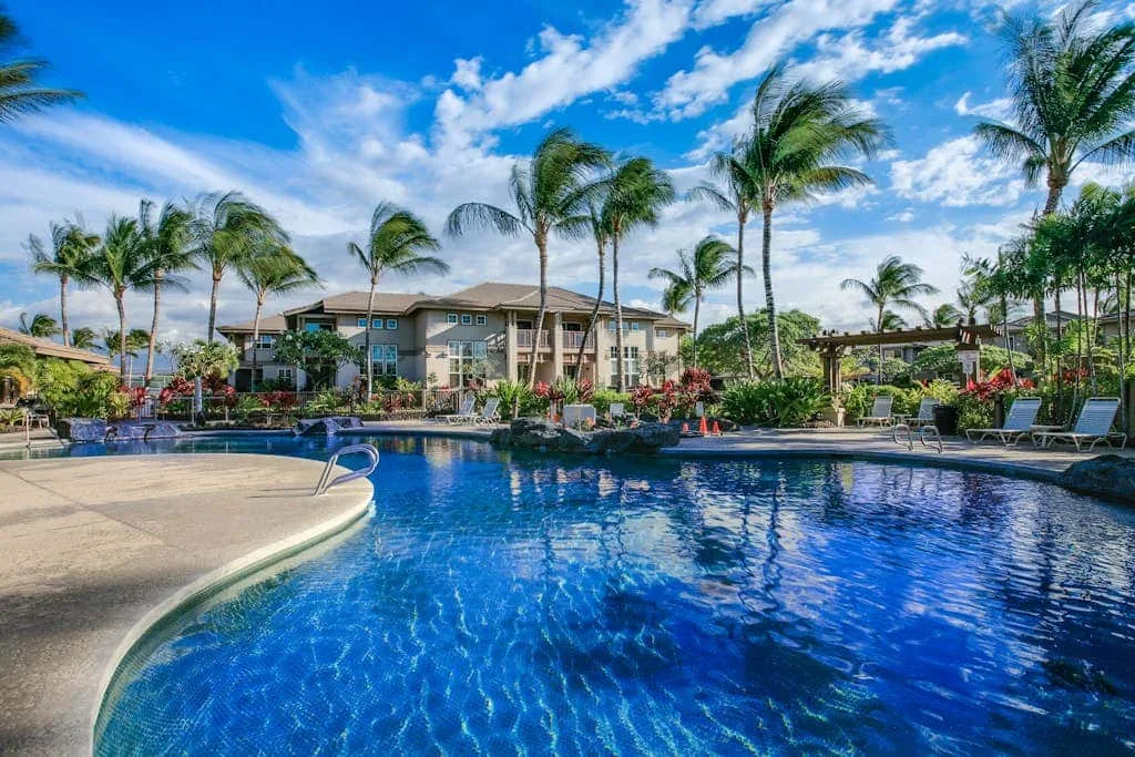 A swimming pool sits among palm trees and landscaped gardens.