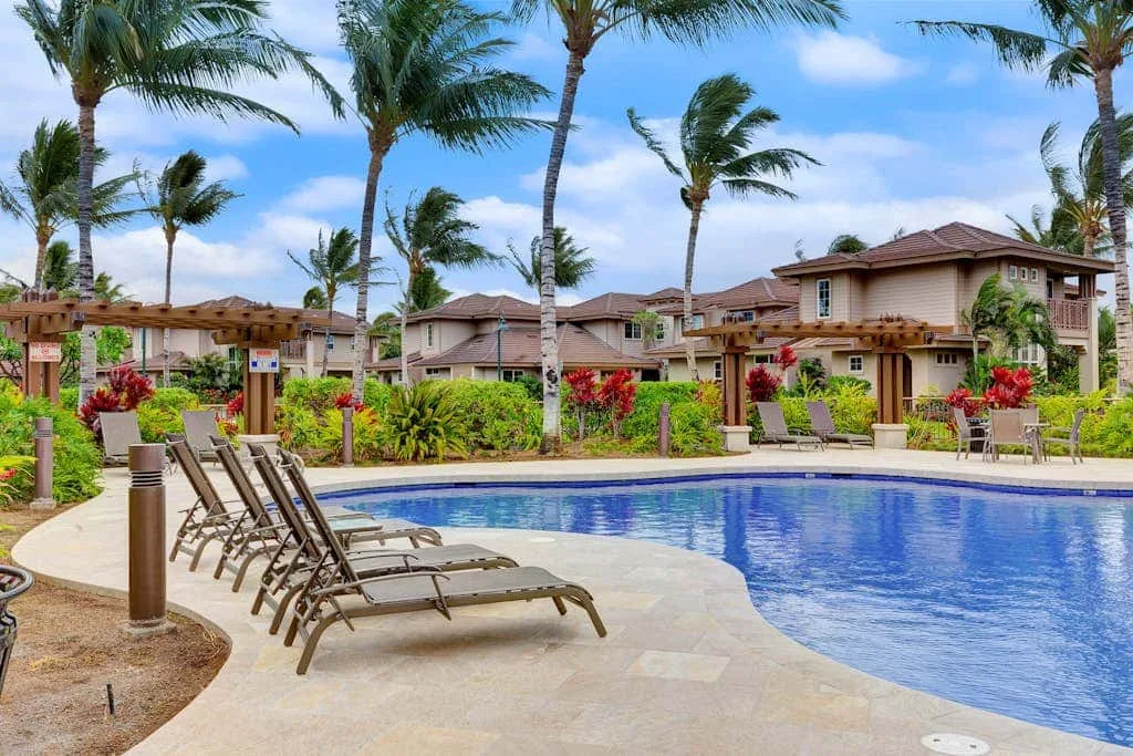 A swimming pool with lounge seating sits among palm trees and landscaped greenery.