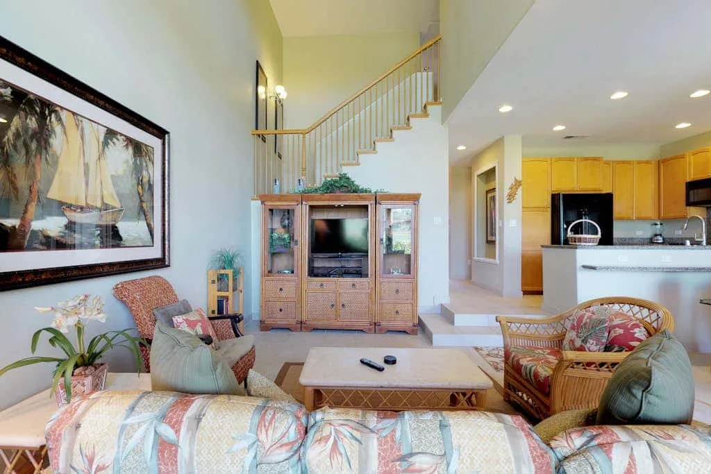 A living room with seating, a television cabinet, and a staircase beside the kitchen.