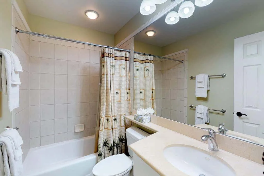 A bathroom with a bathtub, shower curtain, and sink beneath a large mirror.