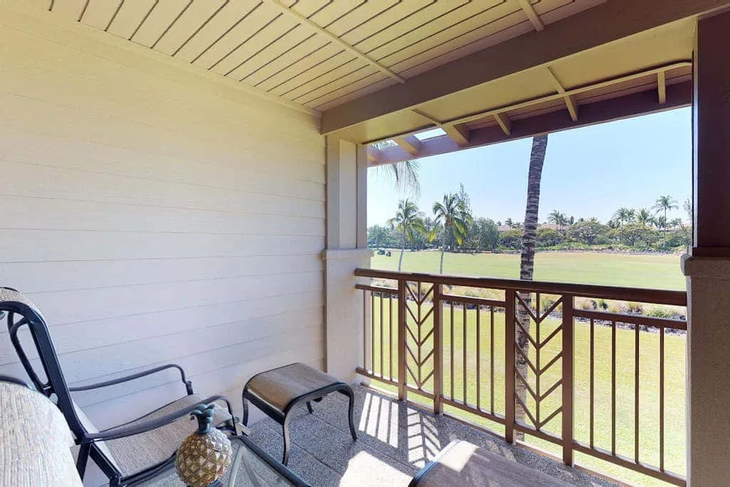 A covered balcony with seating overlooks a grassy landscape and palm trees.