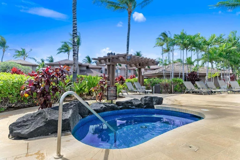 A swimming pool sits among tropical plants and palm trees.