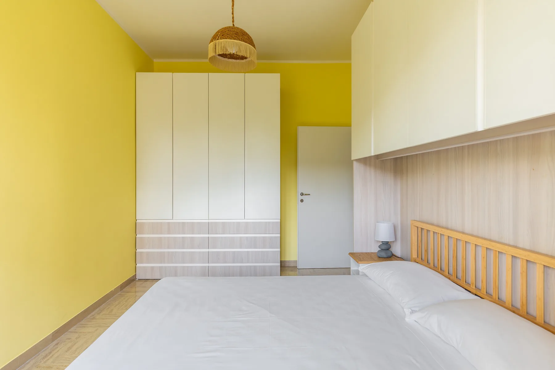 Un dormitorio con una cama junto a un cabecero de madera y armarios blancos.