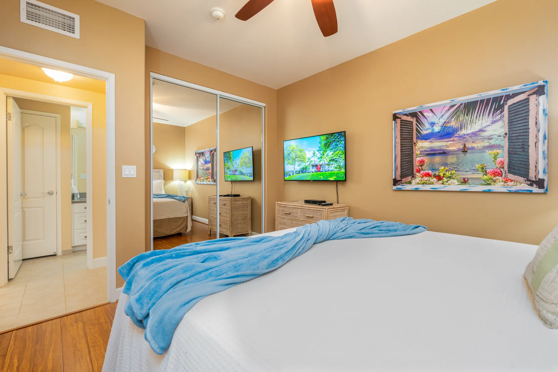 A bedroom with a bed, mirrored closet doors, and a television.