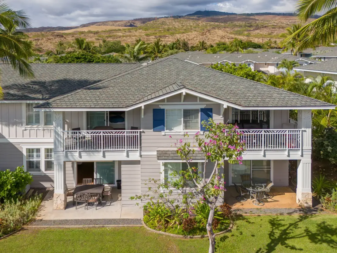 A two-story house with balconies overlooks a landscaped yard and distant hills.