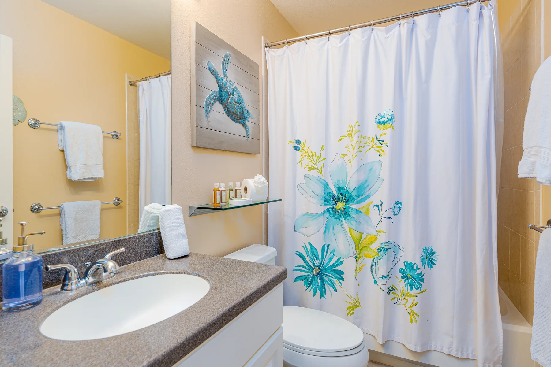 A bathroom with a sink, toilet, and floral shower curtain.