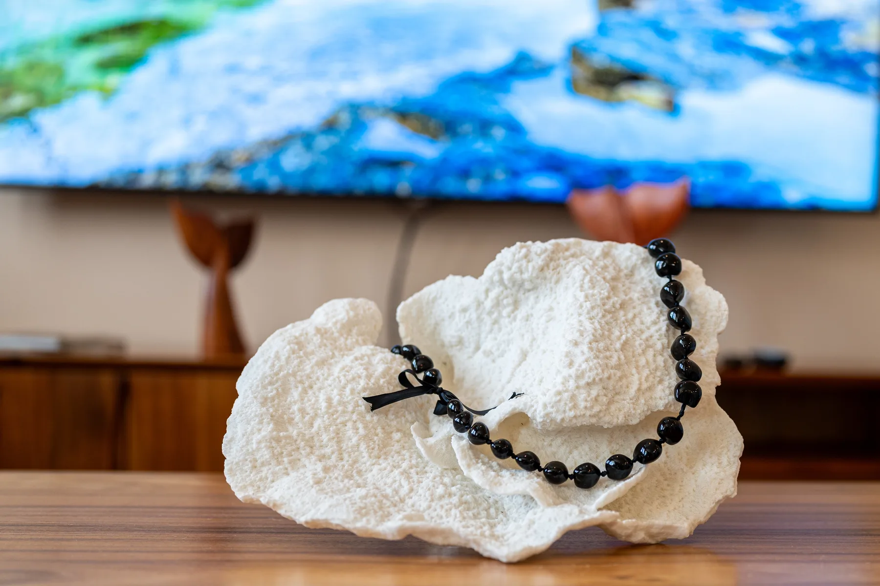A beaded necklace rests on a white coral-shaped display in front of a colorful screen.